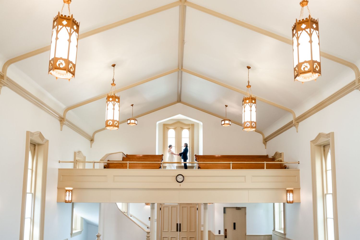 A bright white church interior with vaulted ceilings and hanging pendant lights creates an elegant atmosphere. White Memorial Chapel, SLC.