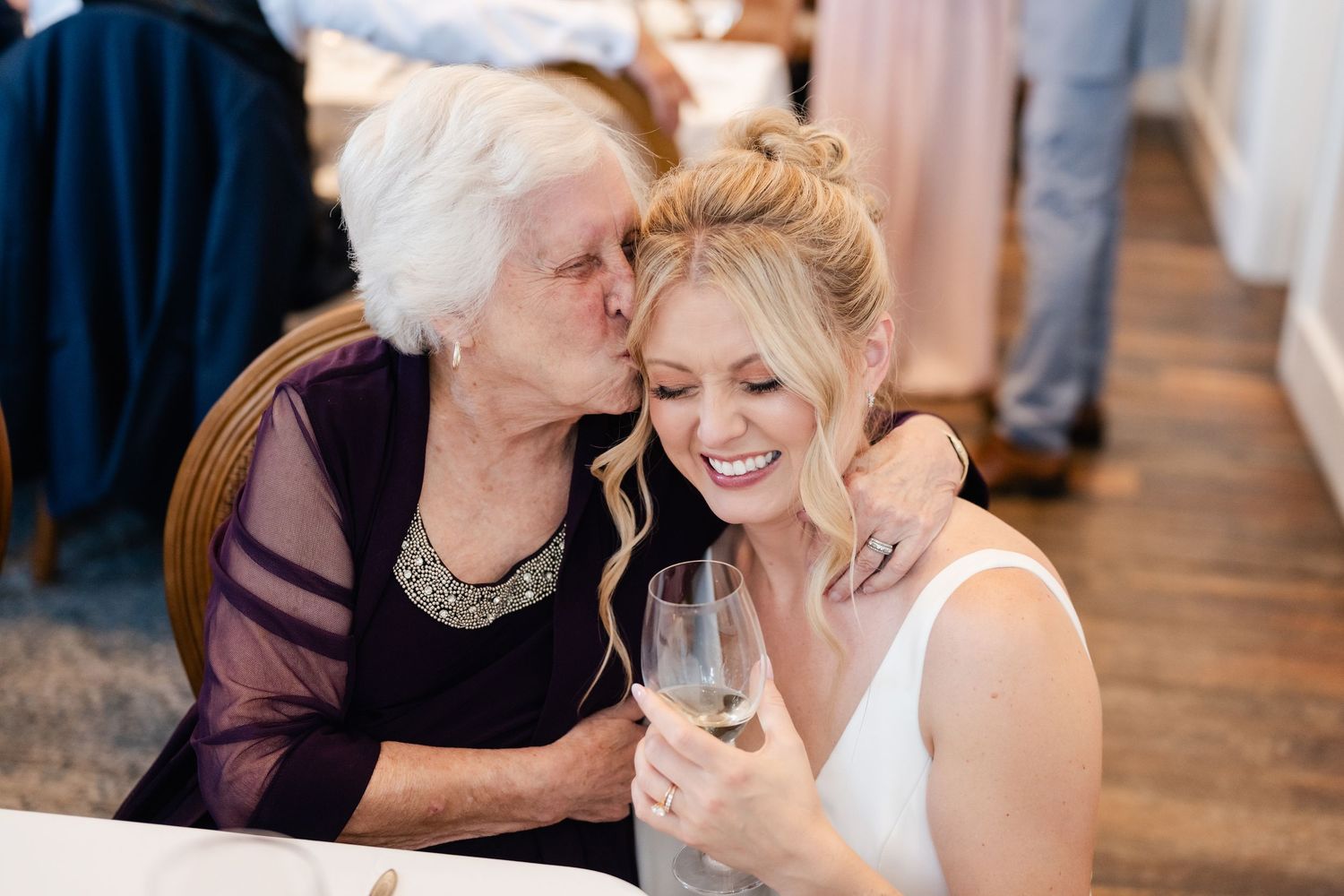 Two people share an affectionate moment while holding wine glasses at a celebration.