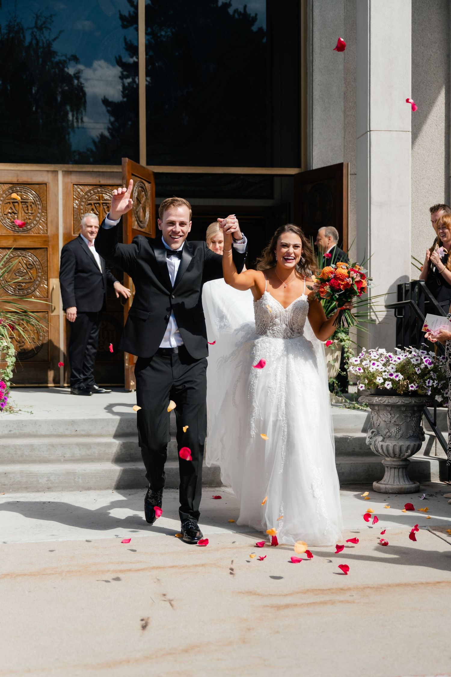 Wedding party members walk down stone steps while rose petals fall at a greek orthodox wedding in Salt Lake City. Utah wedding photographer.