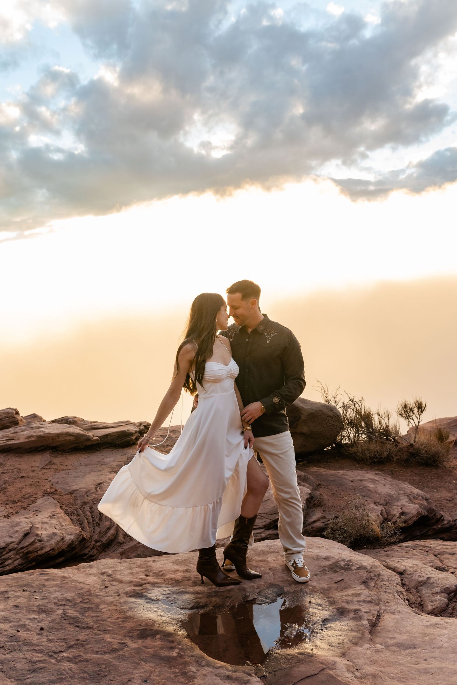 A couple shares romantic moments on red rock formations during sunset in a desert landscape.