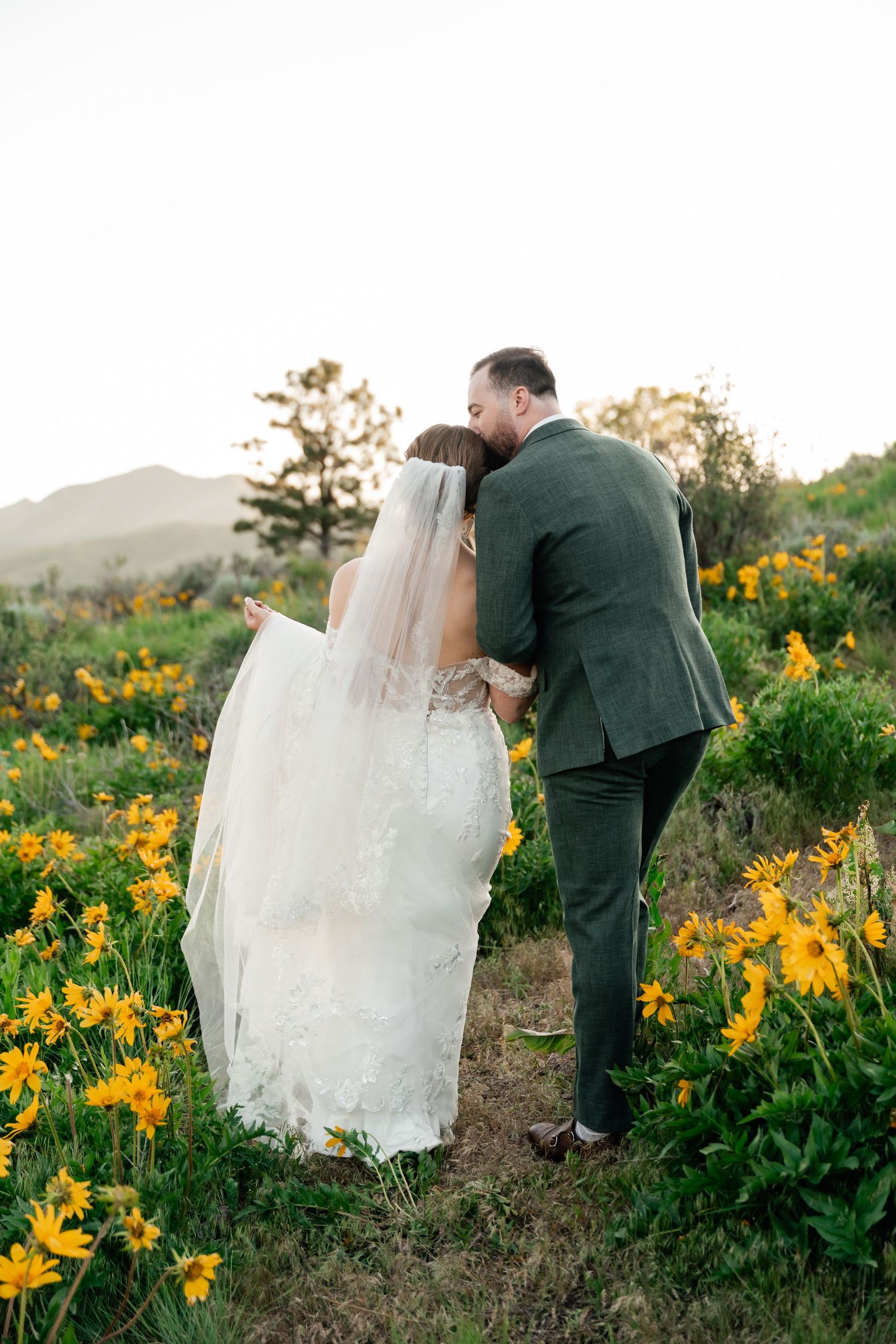 Intimate wedding moment captured among yellow wildflowers with mountains in background.