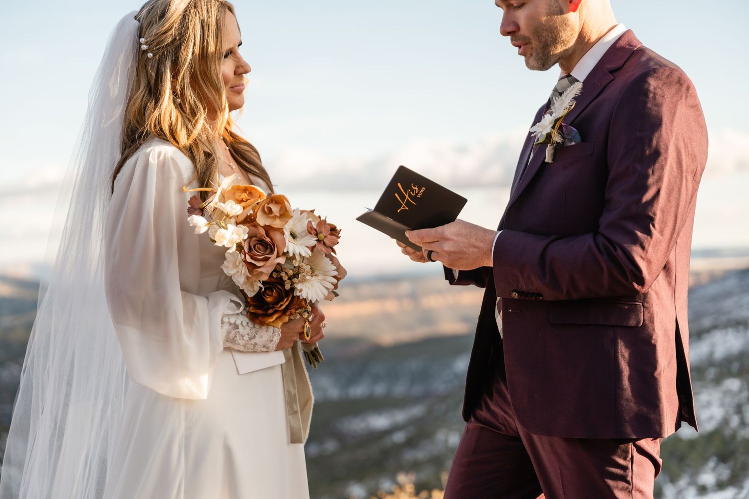 A couple reads their vows against a mountainous backdrop during an outdoor ceremony.