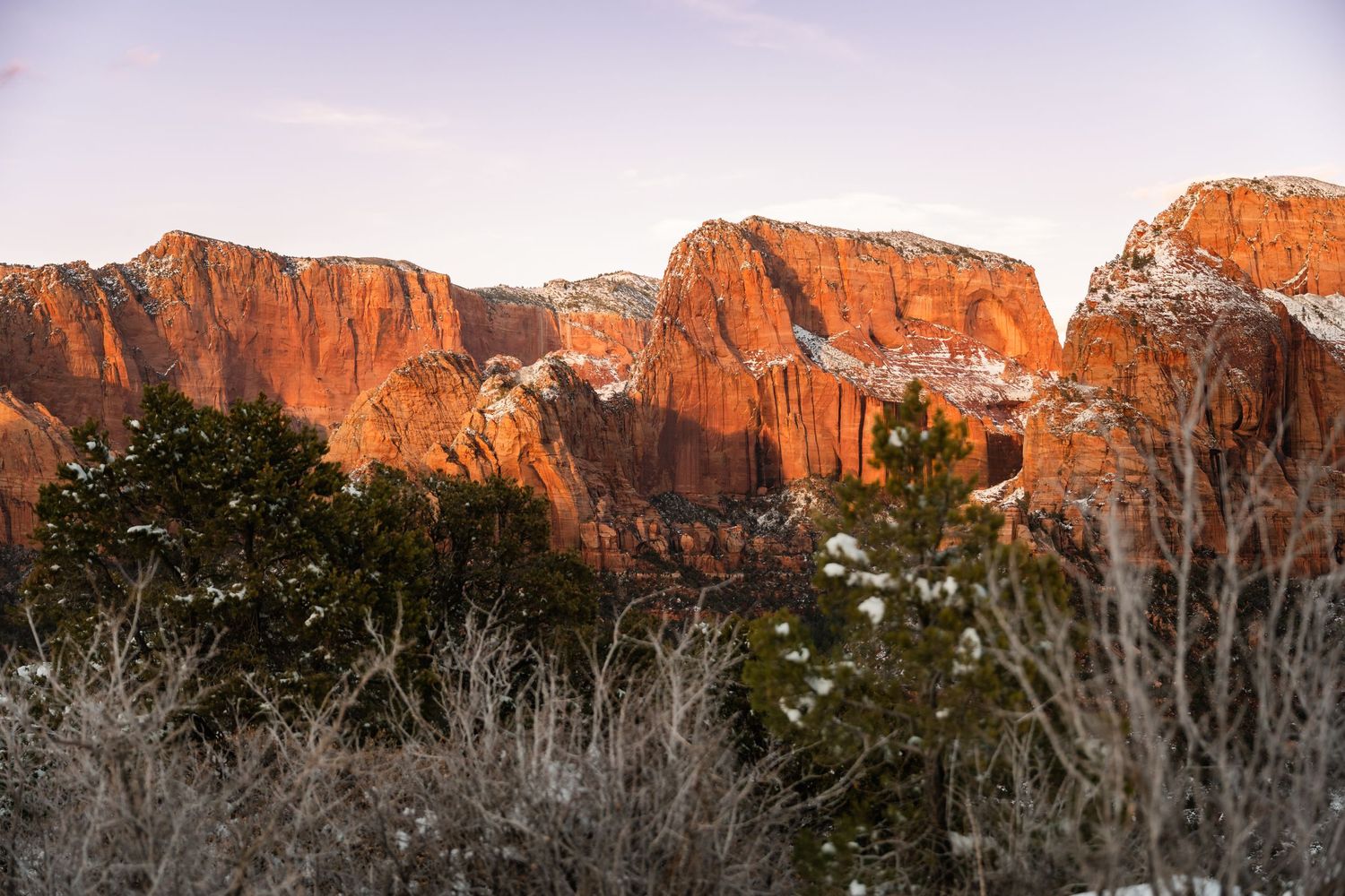 Panoramic view of snow-dusted red rock cliffs glowing in warm sunset light.