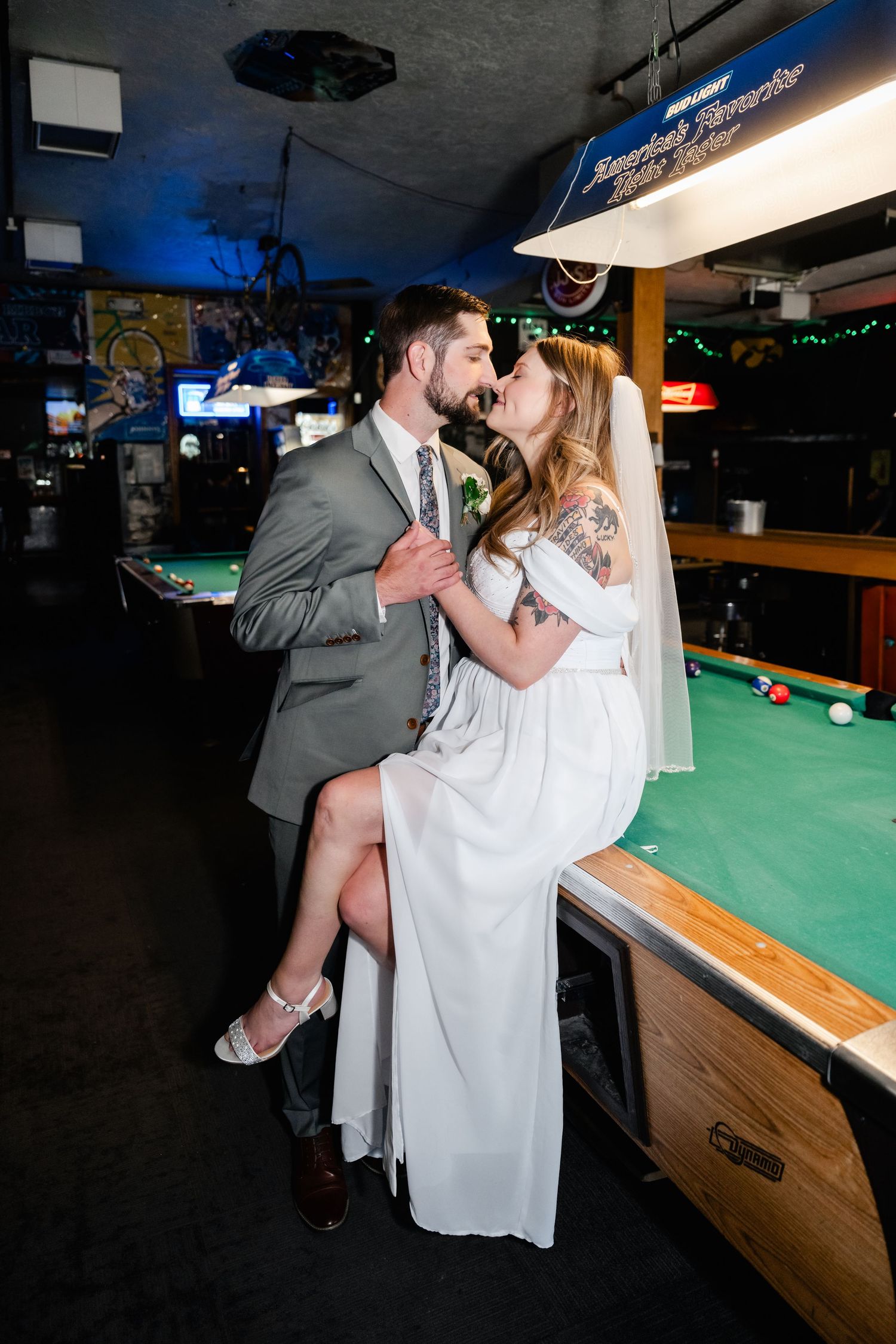 A couple embraces near a pool table in a casual bar setting with blue lighting.