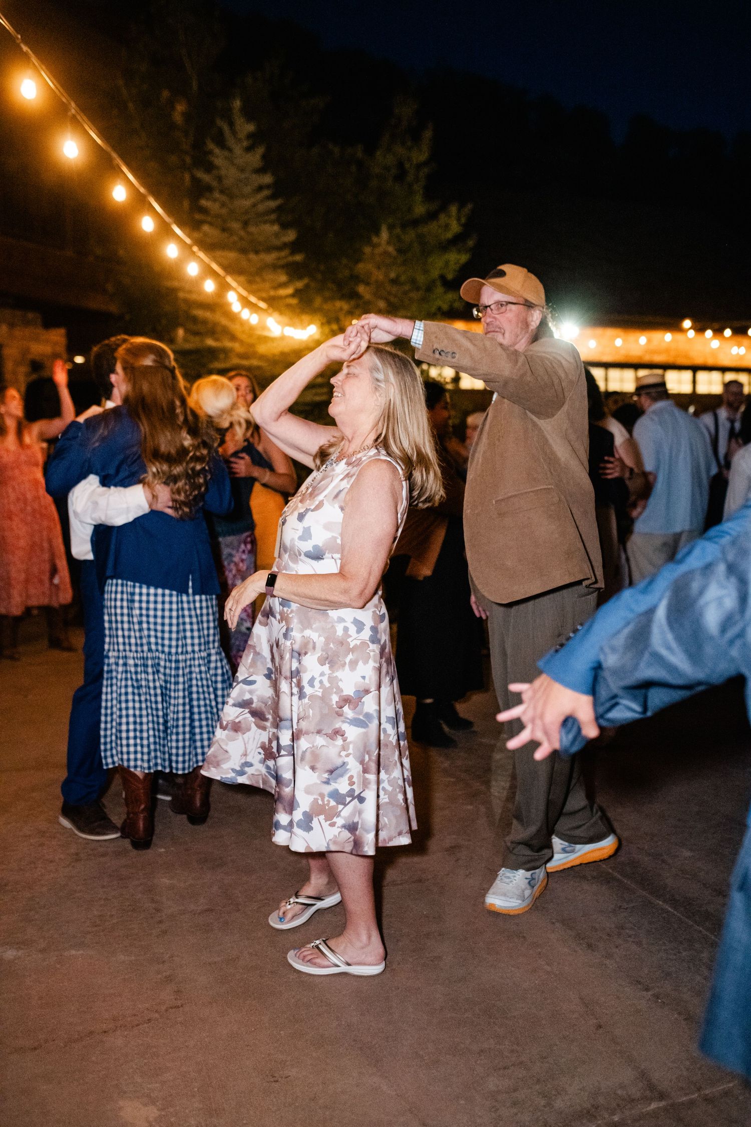 Couples swing dance on an outdoor dance floor under string lights at night.