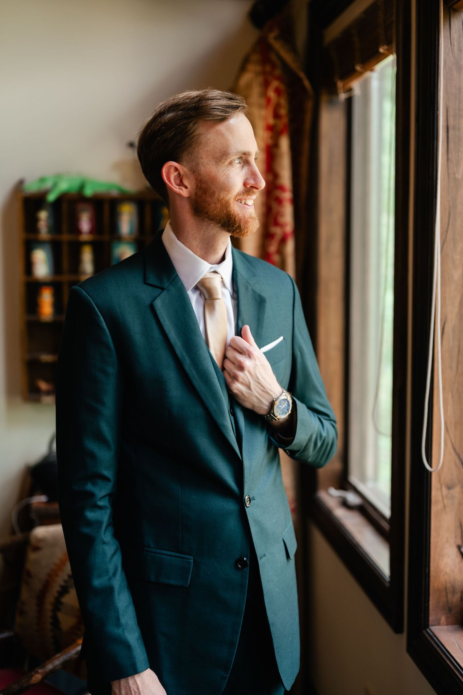A groom in dark suit adjusts his tie while looking out a window in multiple candid shots.