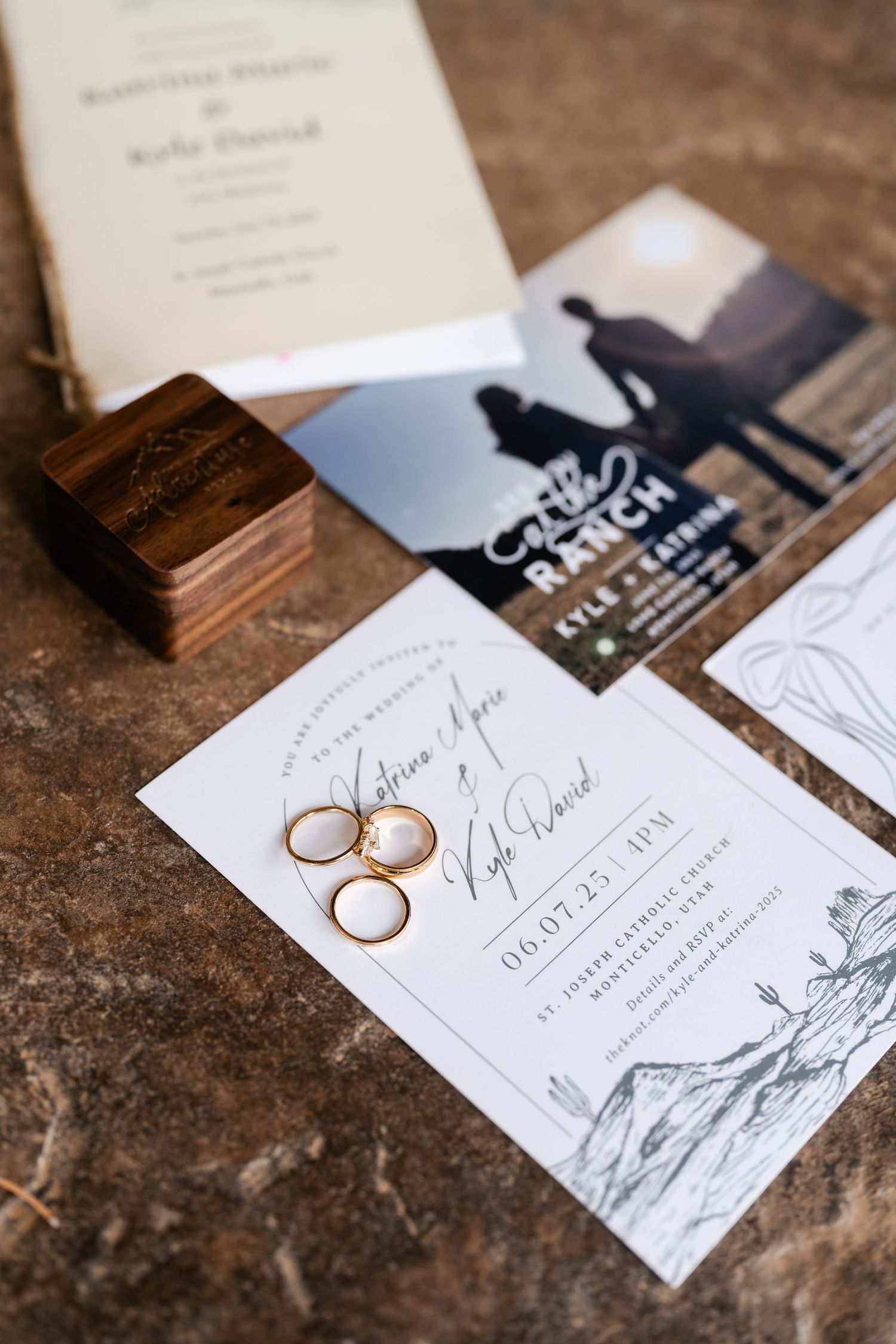 Wedding invitation suite with wooden ring box and gold rings on rustic surface.