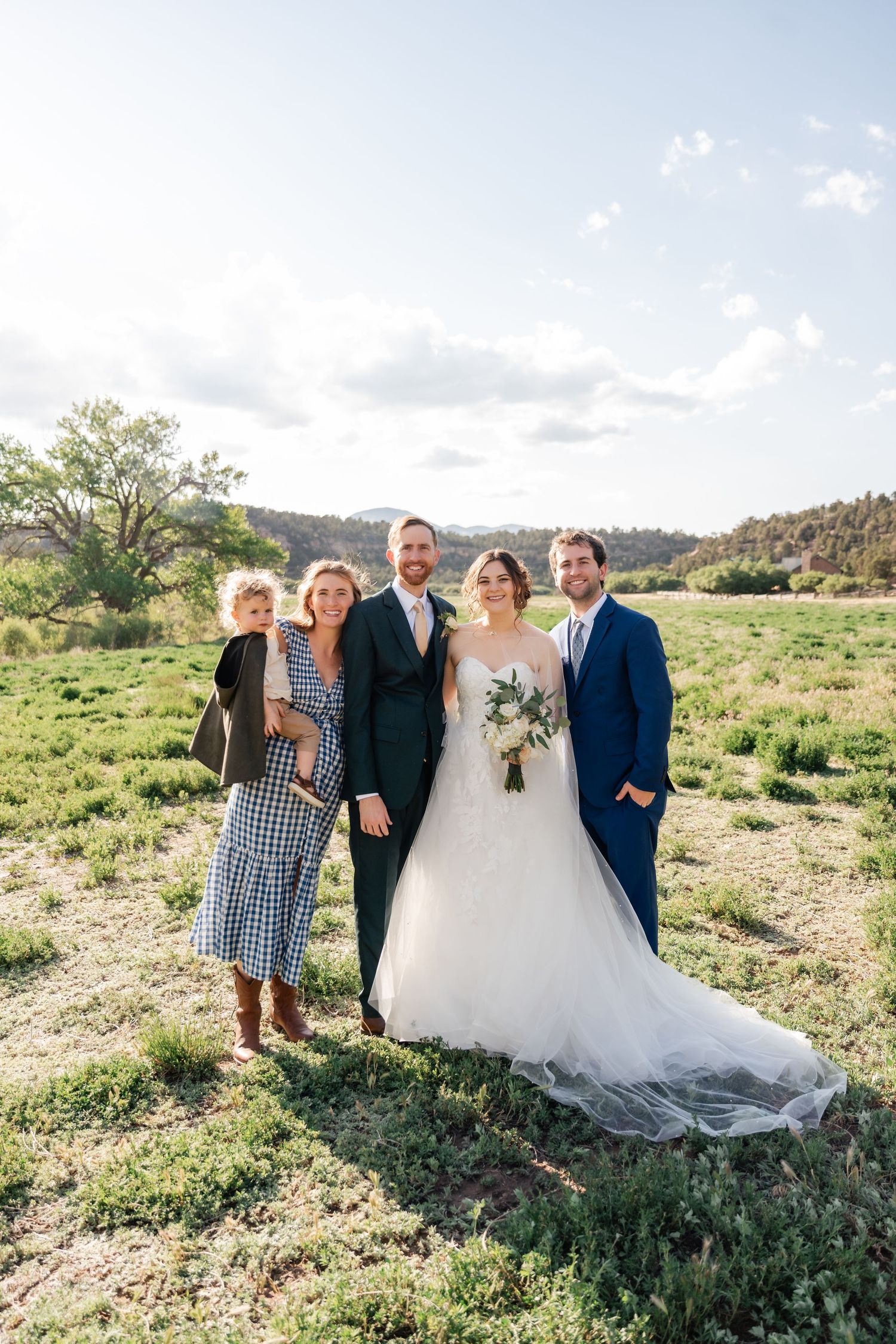 Small wedding group poses together in scenic mountain meadow on sunny afternoon.