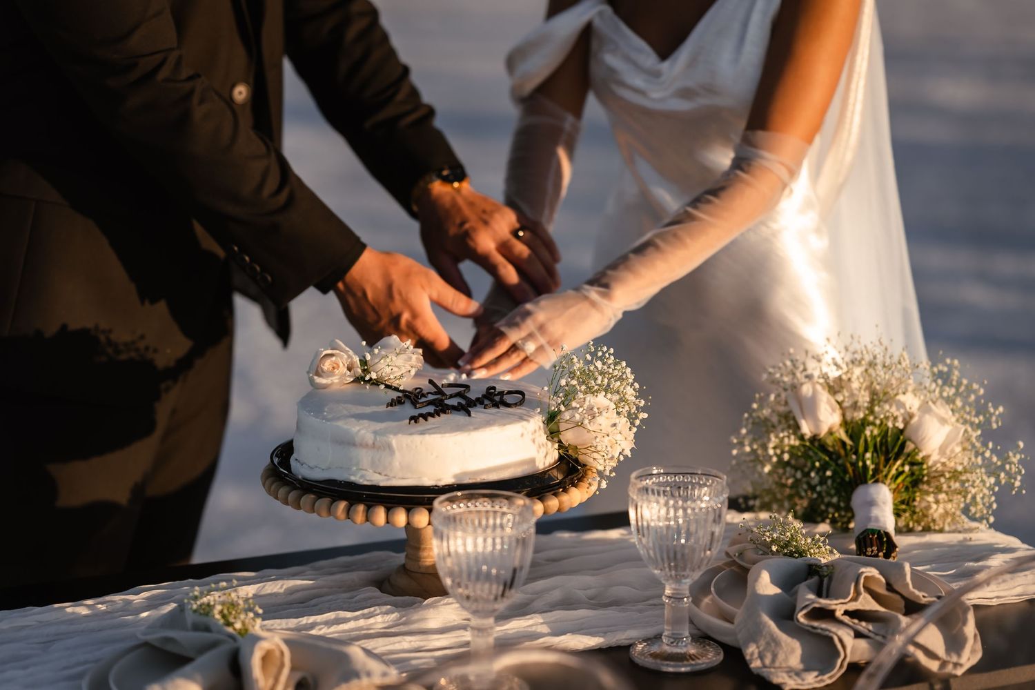 Wedding cake cutting ceremony with crystal glasses on white tablecloth.