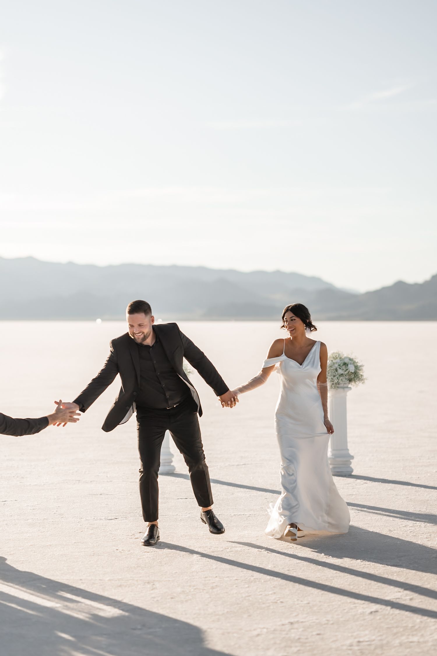 Playful wedding couple dances and celebrates on bright white salt flats.