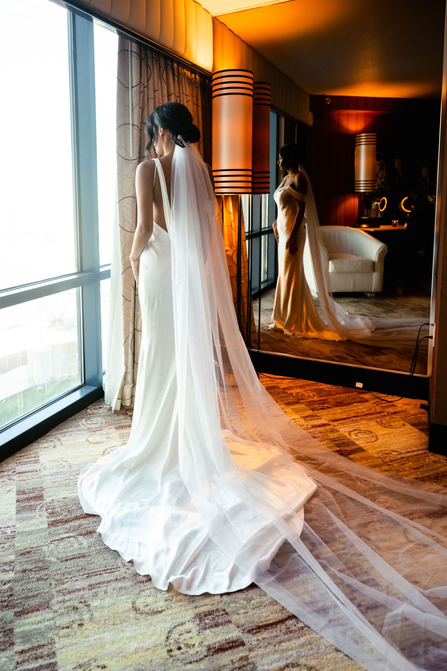 White wedding gown with flowing train photographed in golden light against modern interior.