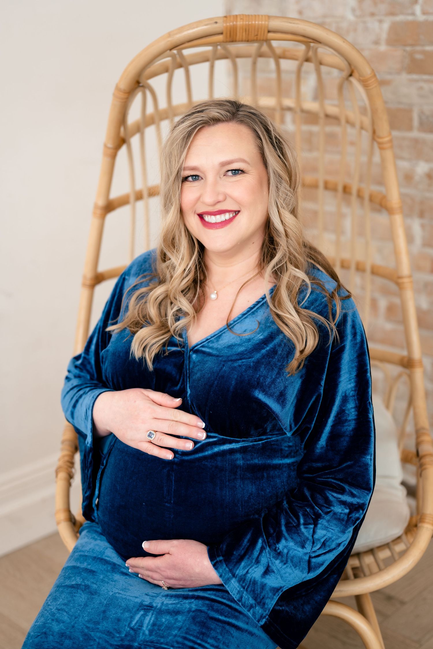 A person in a royal blue velvet dress poses against a brick wall with a rattan chair in a photo series.