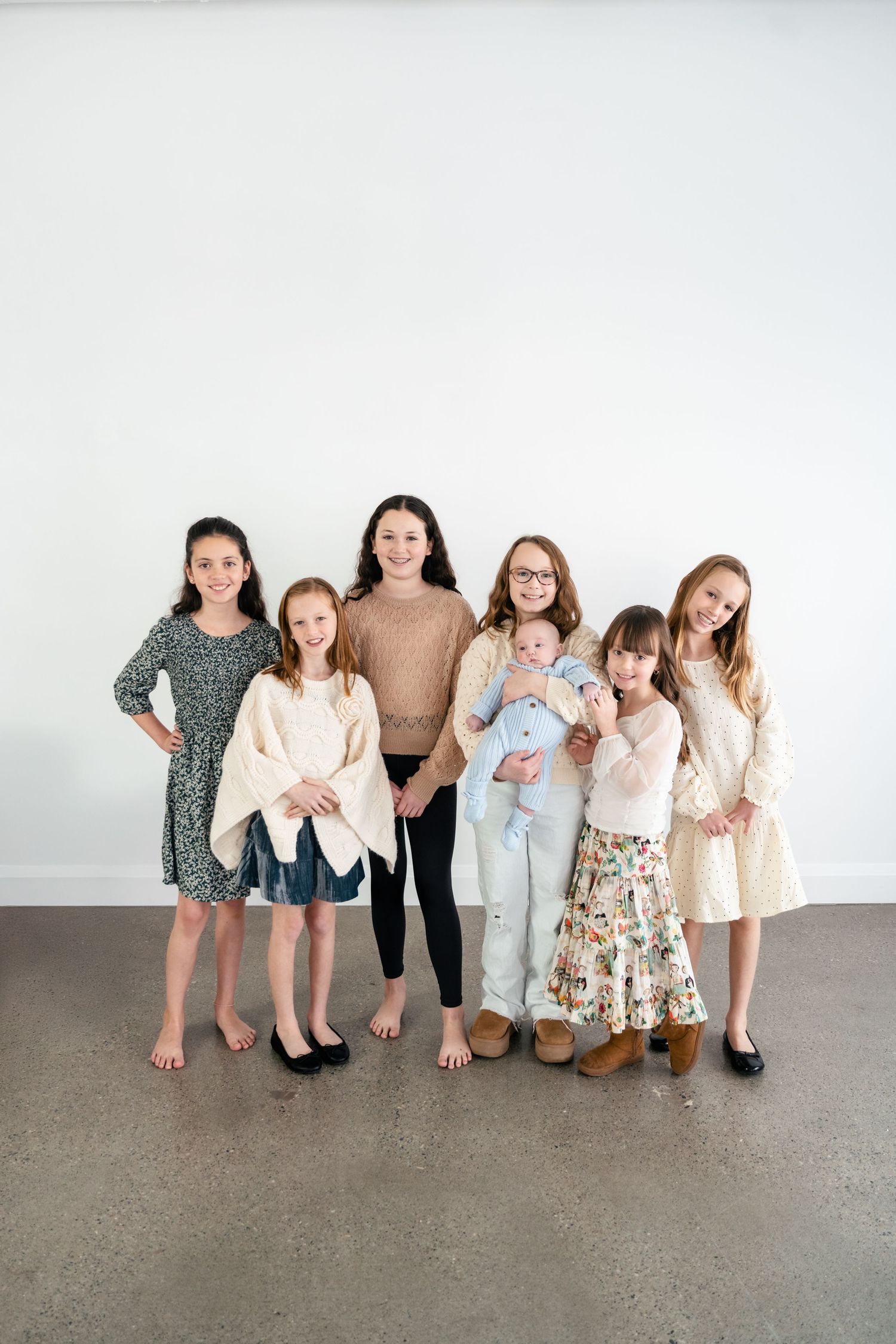 A group of children in casual attire stand together against a white wall in three similar poses.