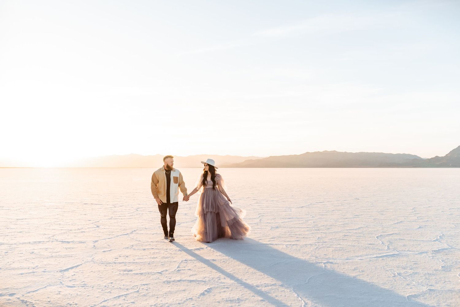Utah Salt Flats Photographer. Romantic couple walking hand in hand across pristine white salt flats at sunset.