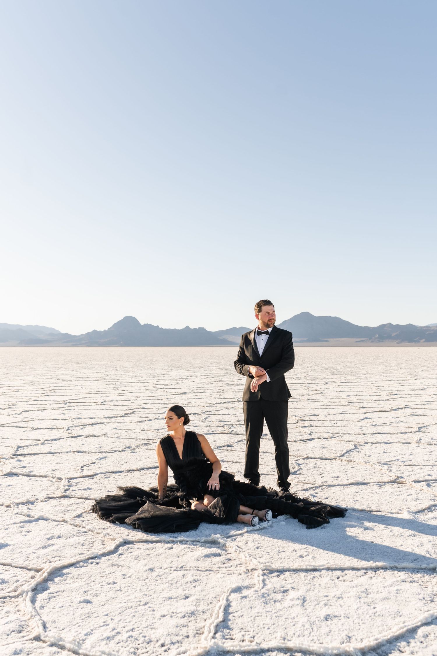Salt Flats Photographer. Two people in formal attire pose dramatically on the white salt flats with mountains in the background.