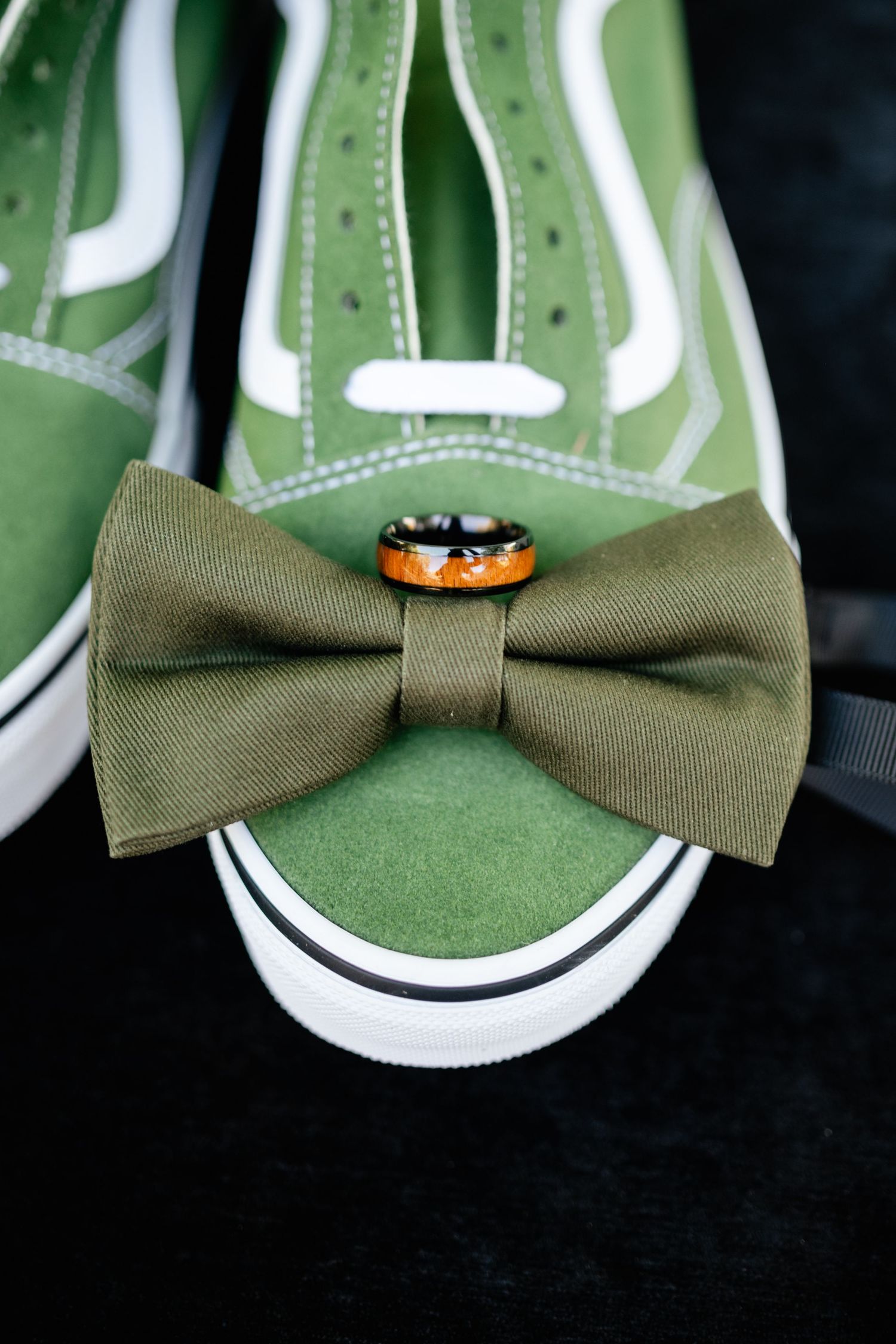 Green Vans sneaker with olive bow tie and gold ring displayed on dark background, emphasizing wedding accessories.