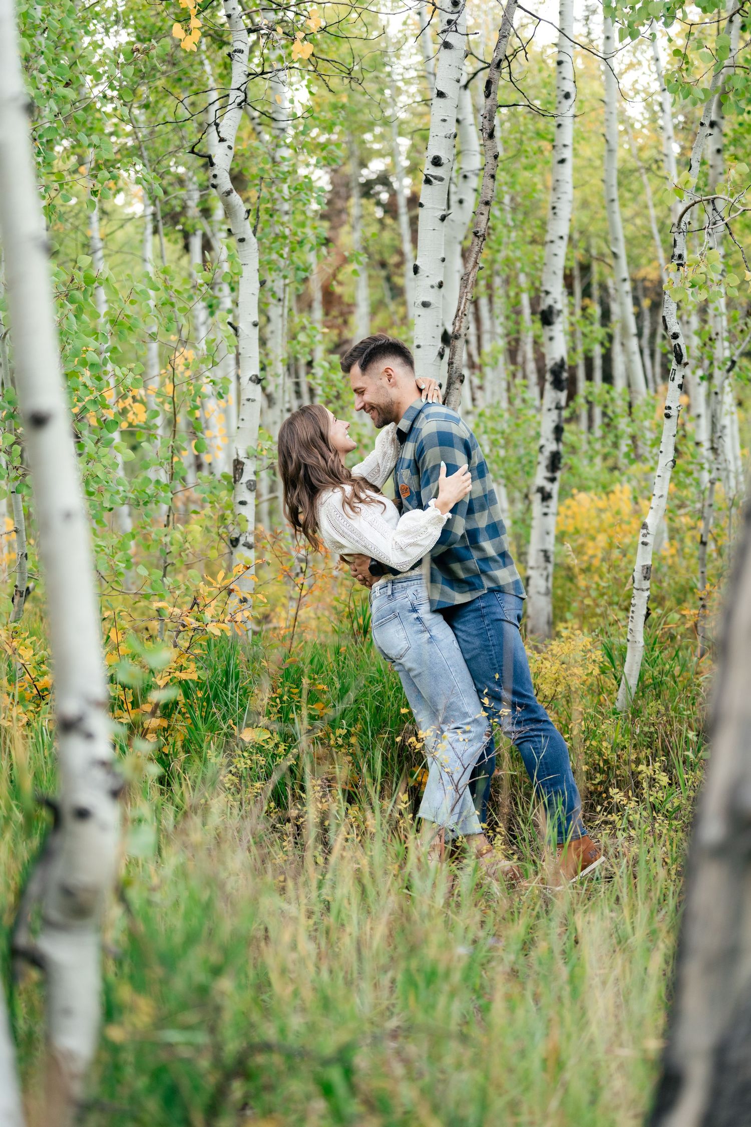 A romantic couple embraces in a sunlit grove of birch trees with golden autumn leaves.