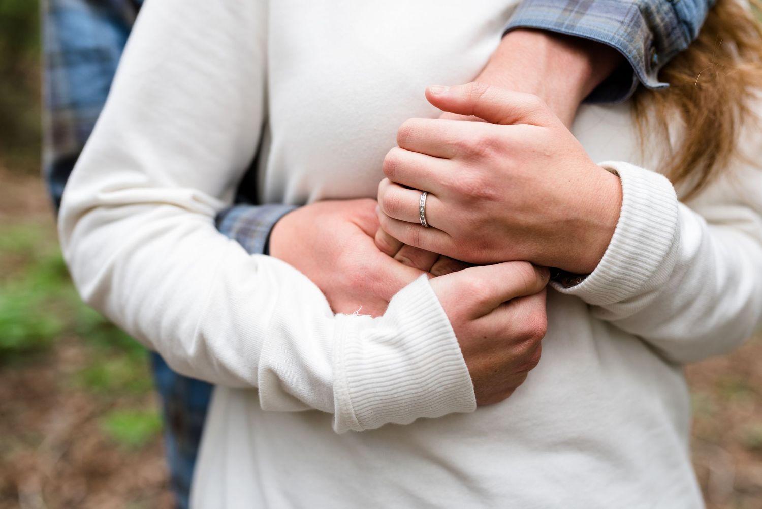 Close-up of hands showing off an engagement ring against a cream sweater.