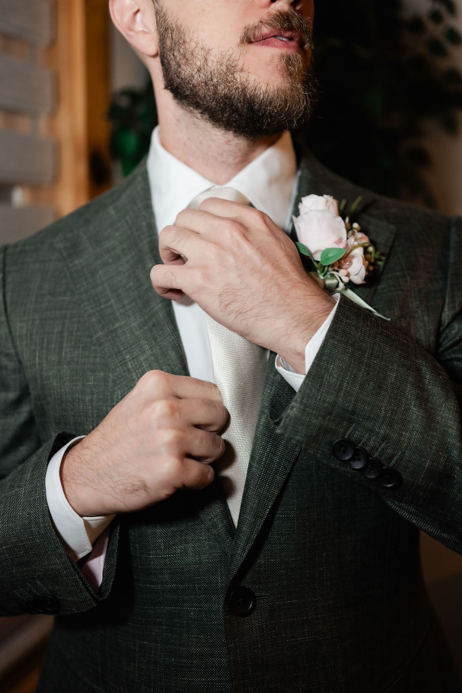 Close-up shots of a groom adjusting his tie while wearing a dark suit with boutonniere.