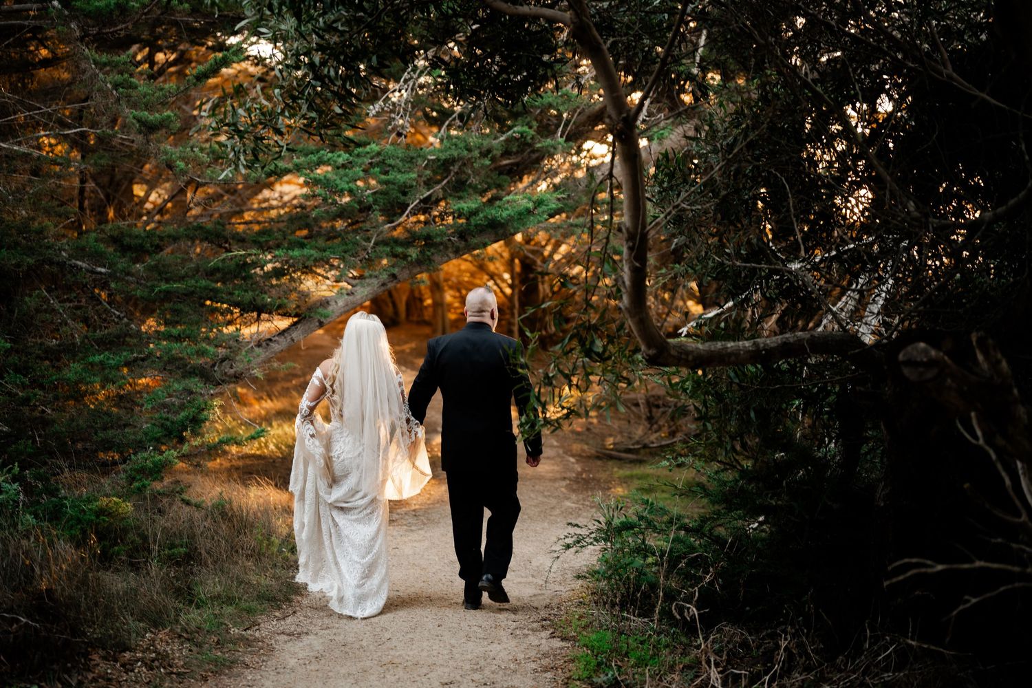 Wedding couple walking through forest path during sunset golden hour.