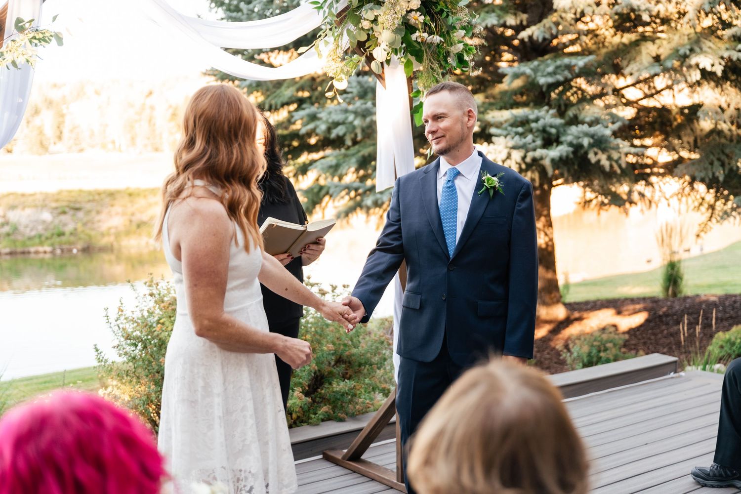 Wedding guests seated outdoors at a ceremony with natural fall foliage and trees in the background.