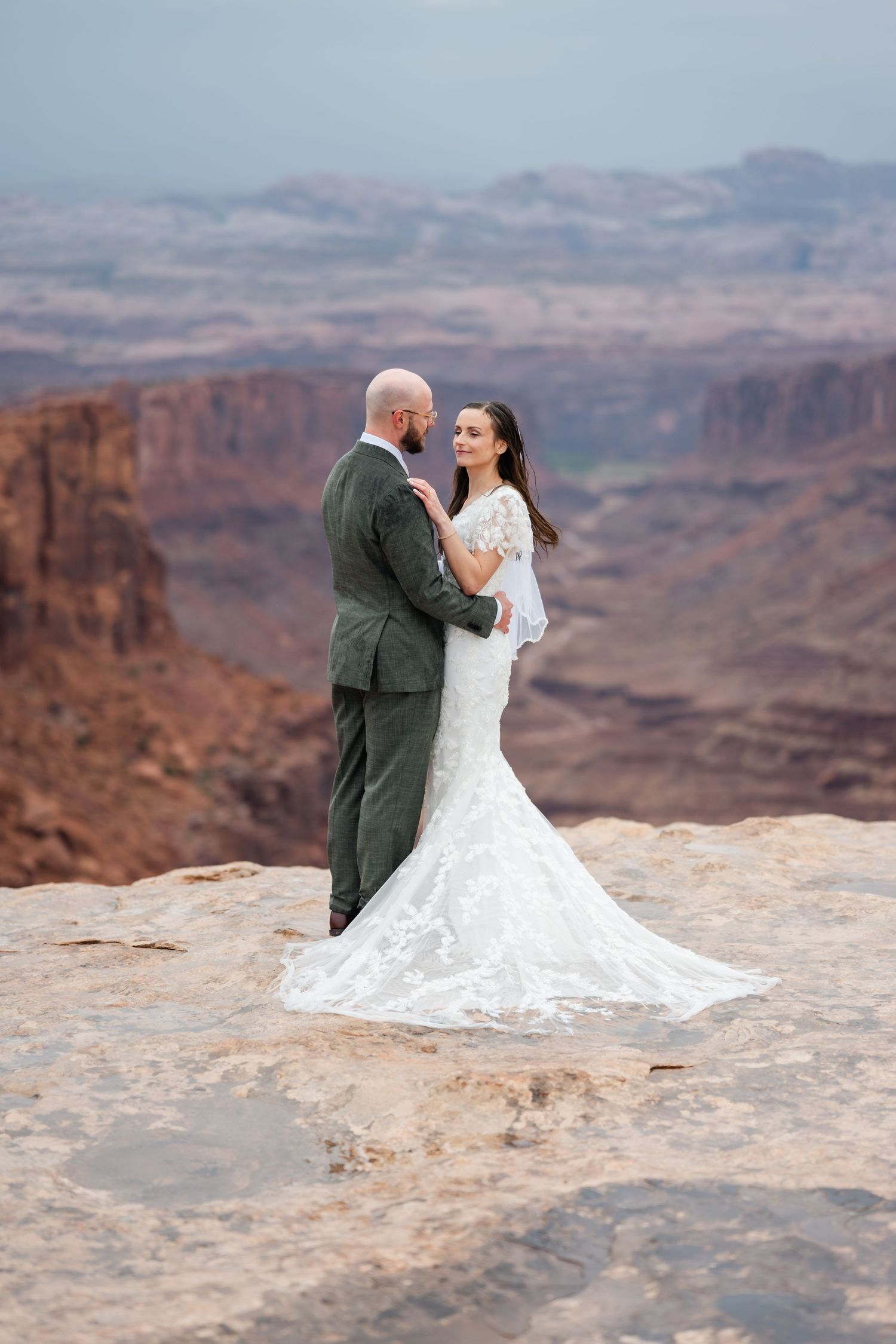 A romantic wedding photoshoot on a dramatic cliff edge overlooking vast desert canyons and red rock formations.