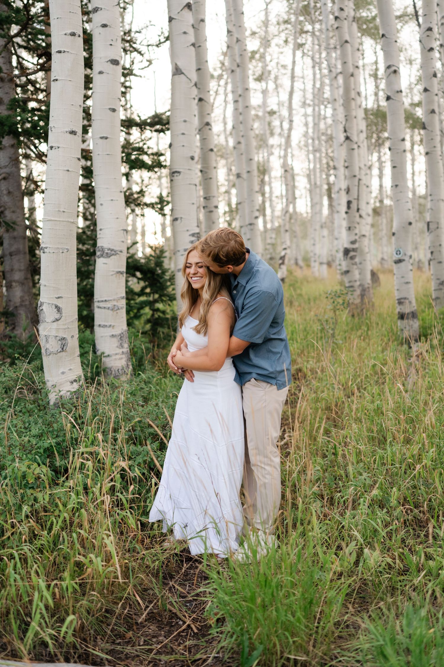 Couple embracing in an aspen grove, woman in white dress smiling, at Guardsman Pass above Park City.