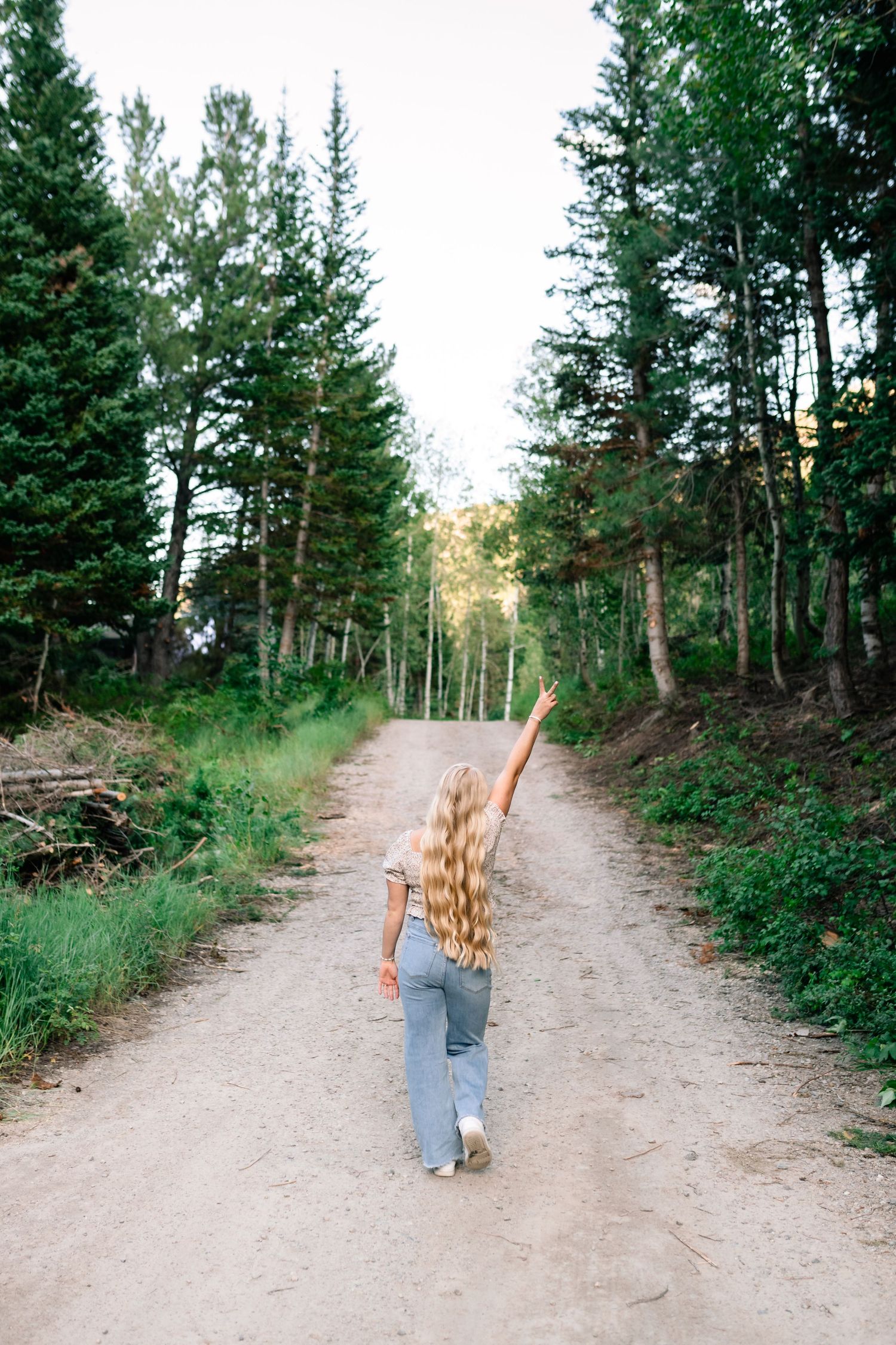 senior girl walking down a dirt road giving a peace sign taken by Coley, Utah Senior Photographer