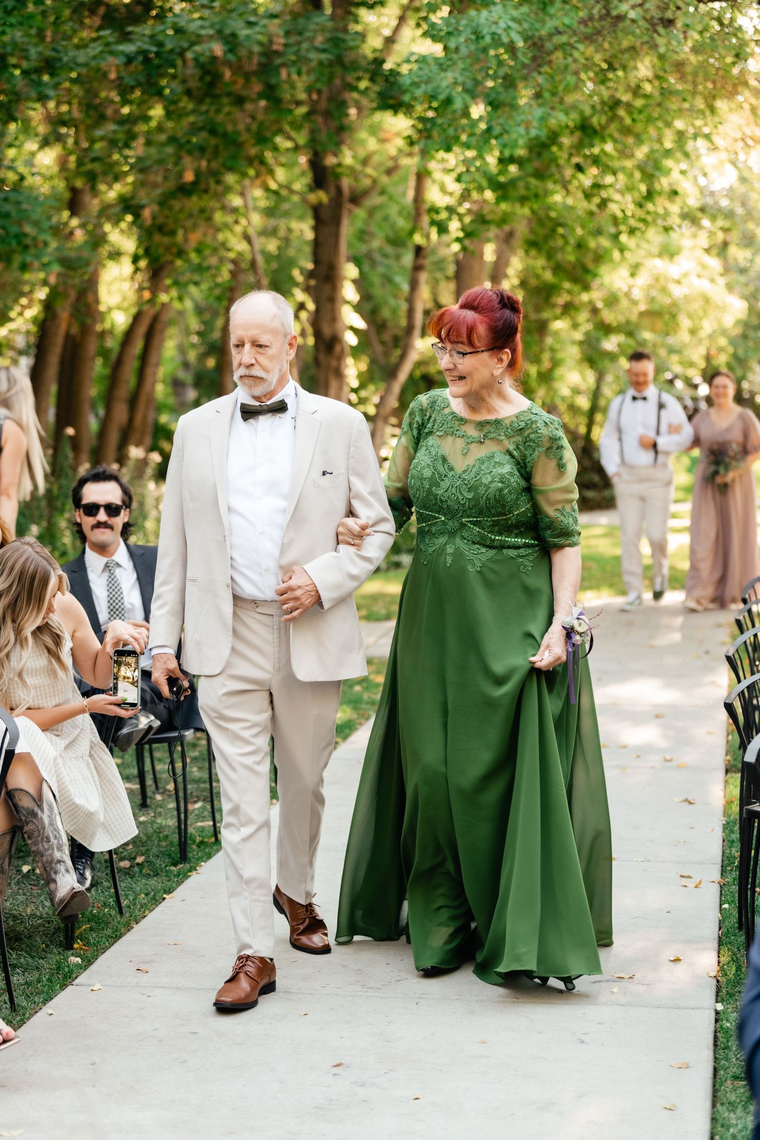 Attendees walking down a garden path, with one wearing a stunning emerald green formal gown.
