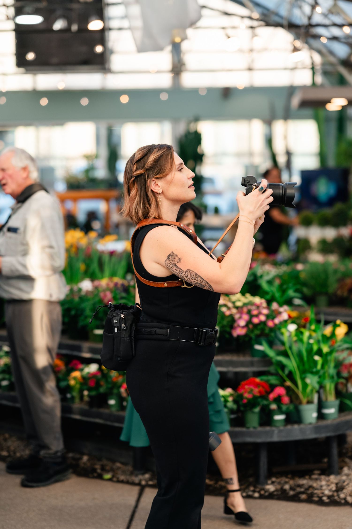 Photographer with a camera taking pictures at a vibrant indoor garden market with colorful flowers and plants on display.