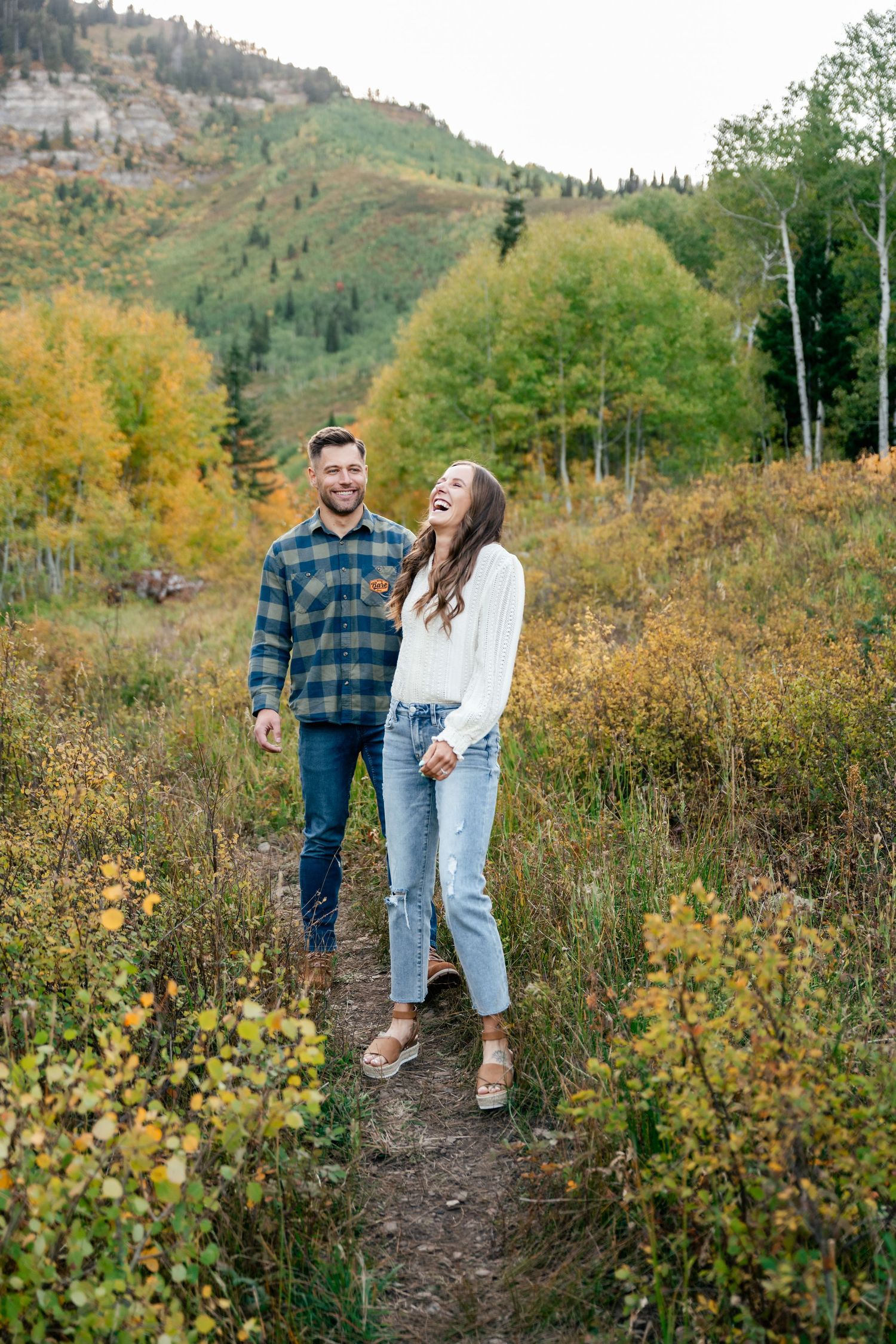 A couple enjoying an autumn hike along a mountain trail surrounded by golden foliage and aspen trees.