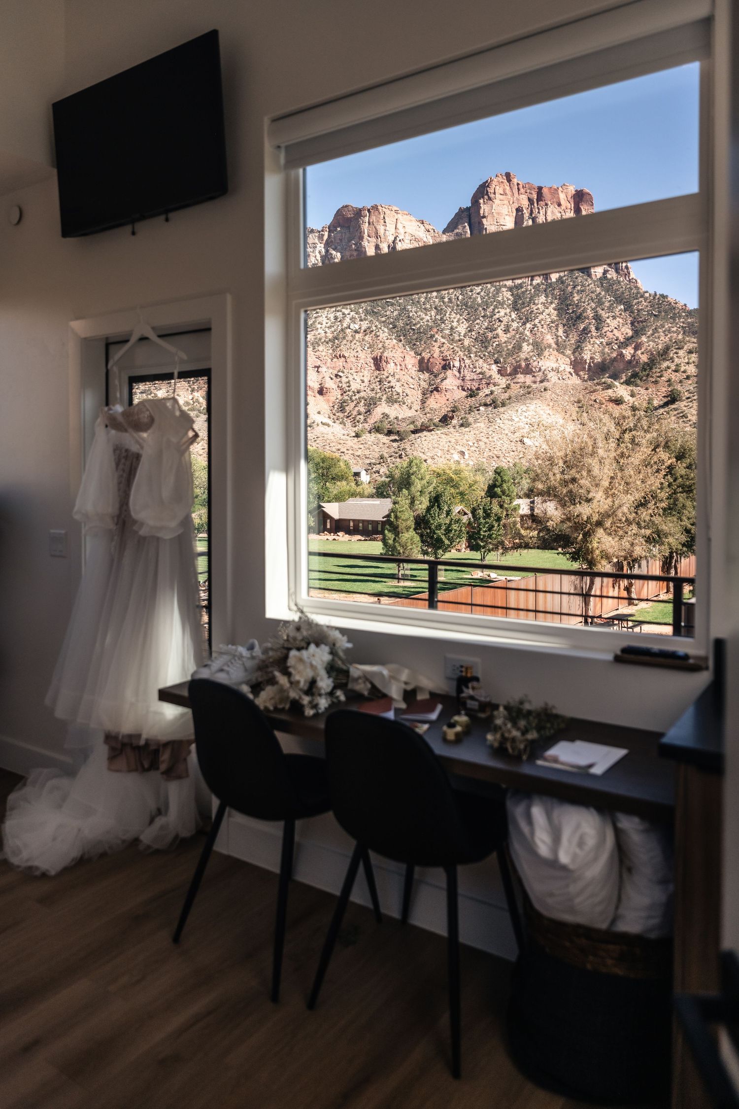 Wedding dress hangs in room with stunning mountain view through large window and black chairs.