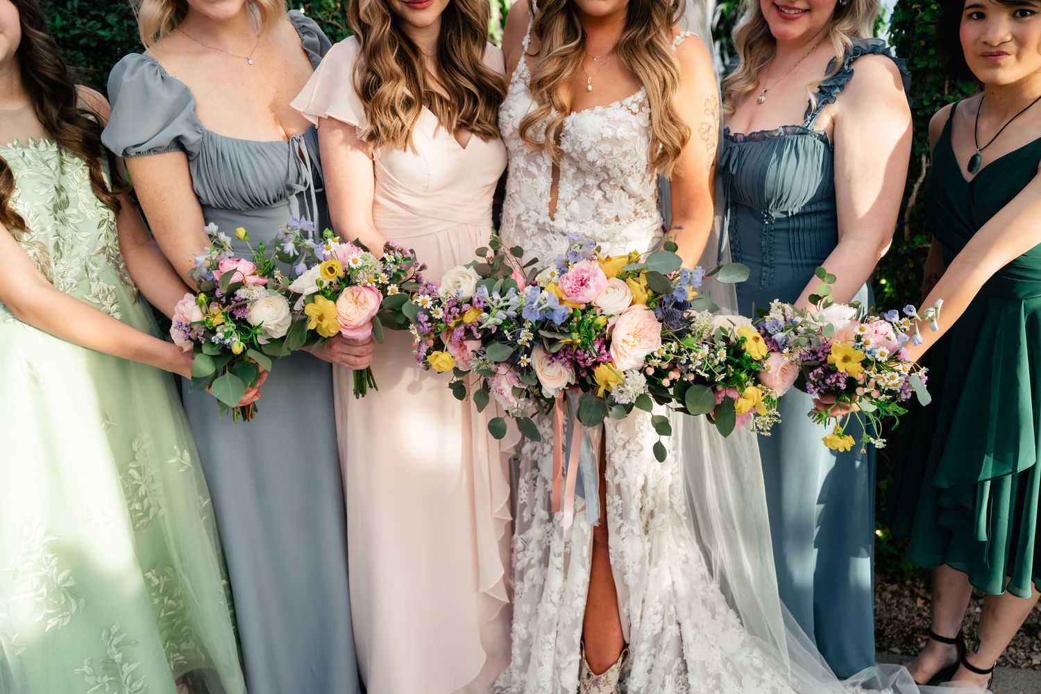 Bridesmaids in mismatched pastel dresses holding colorful wildflower bouquets at a wedding celebration.