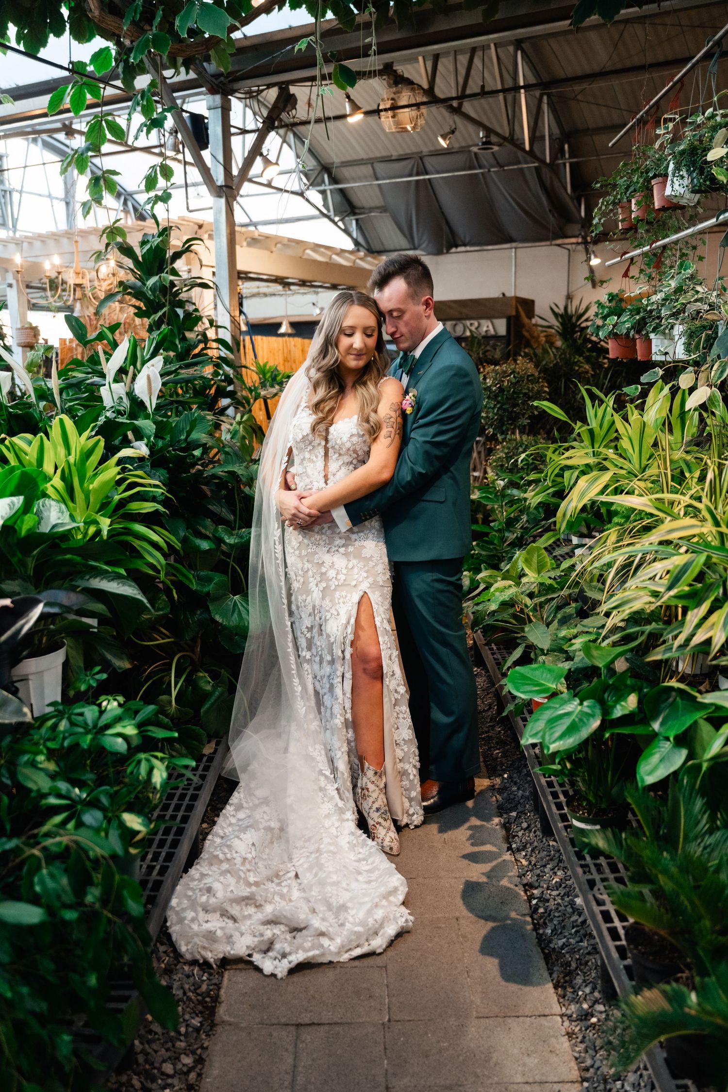 A couple embraces in a romantic greenhouse setting surrounded by lush tropical plants and greenery.