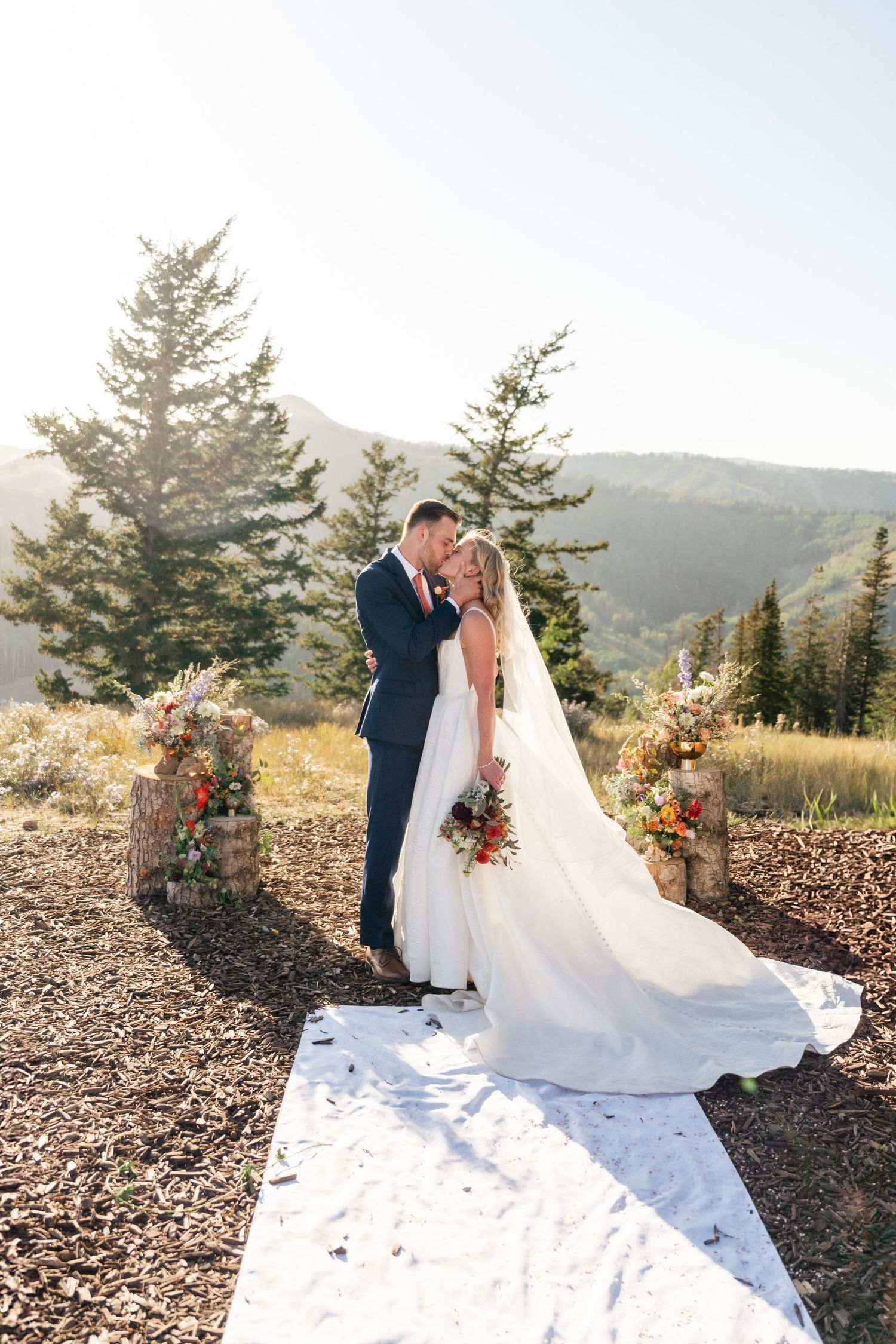A stunning mountaintop wedding ceremony with a white aisle runner and floral arch overlooking mountain vistas at sunset. Park City Wedding.