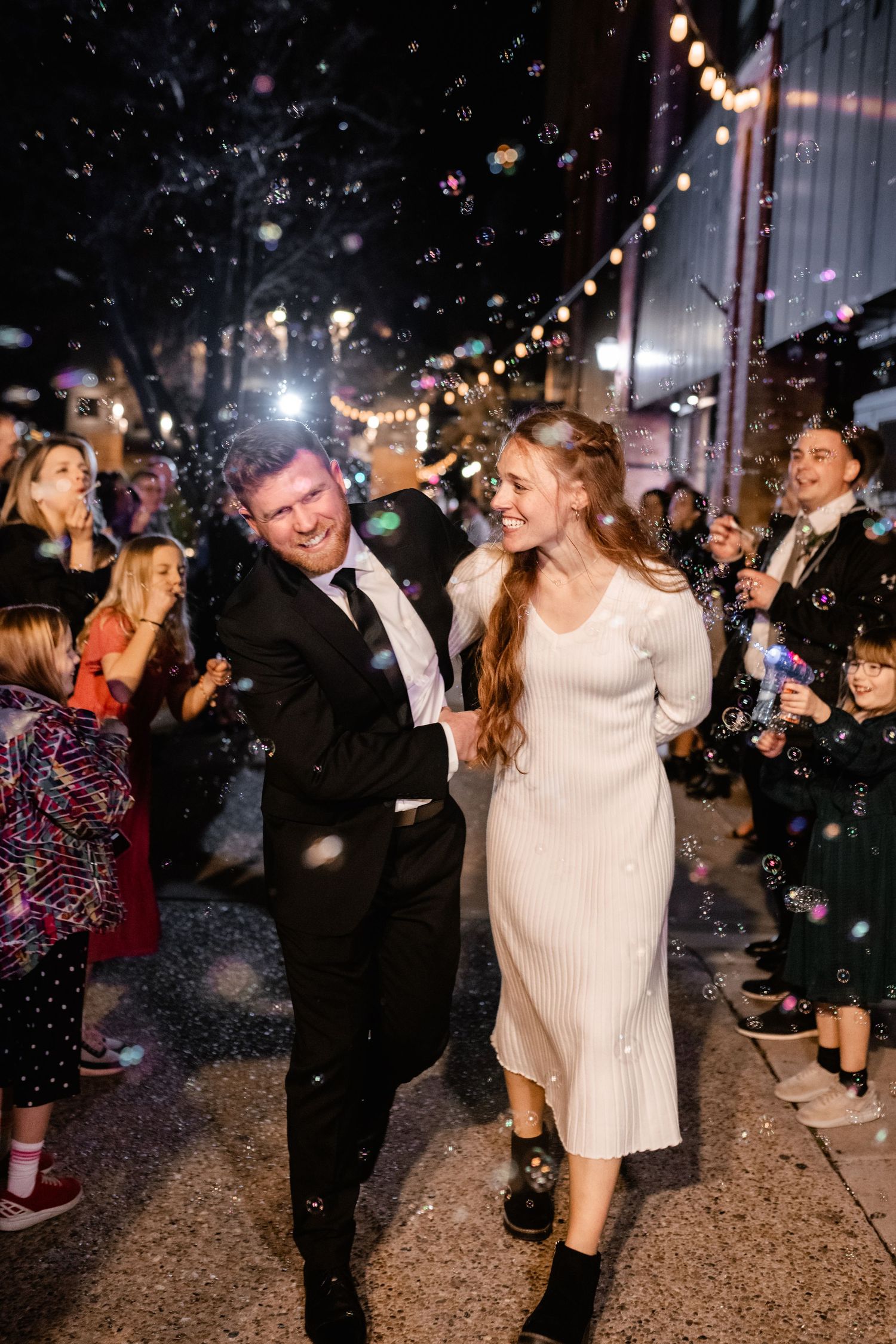 Couple dancing under string lights and bubbles at a festive nighttime celebration.