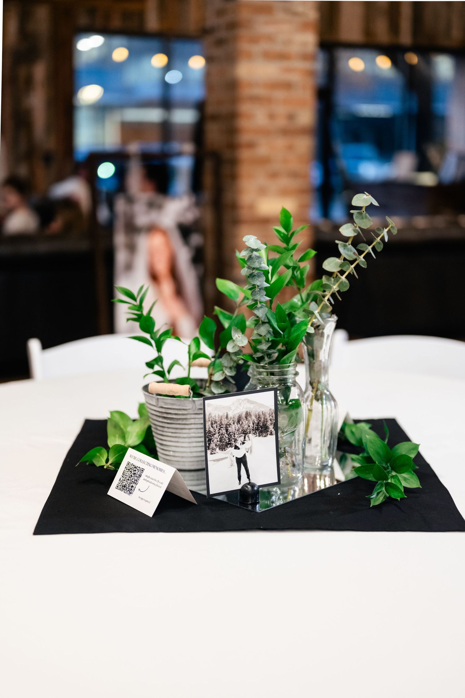 Simple table centerpiece with eucalyptus in tin cans and vintage black and white photos on a white tablecloth.