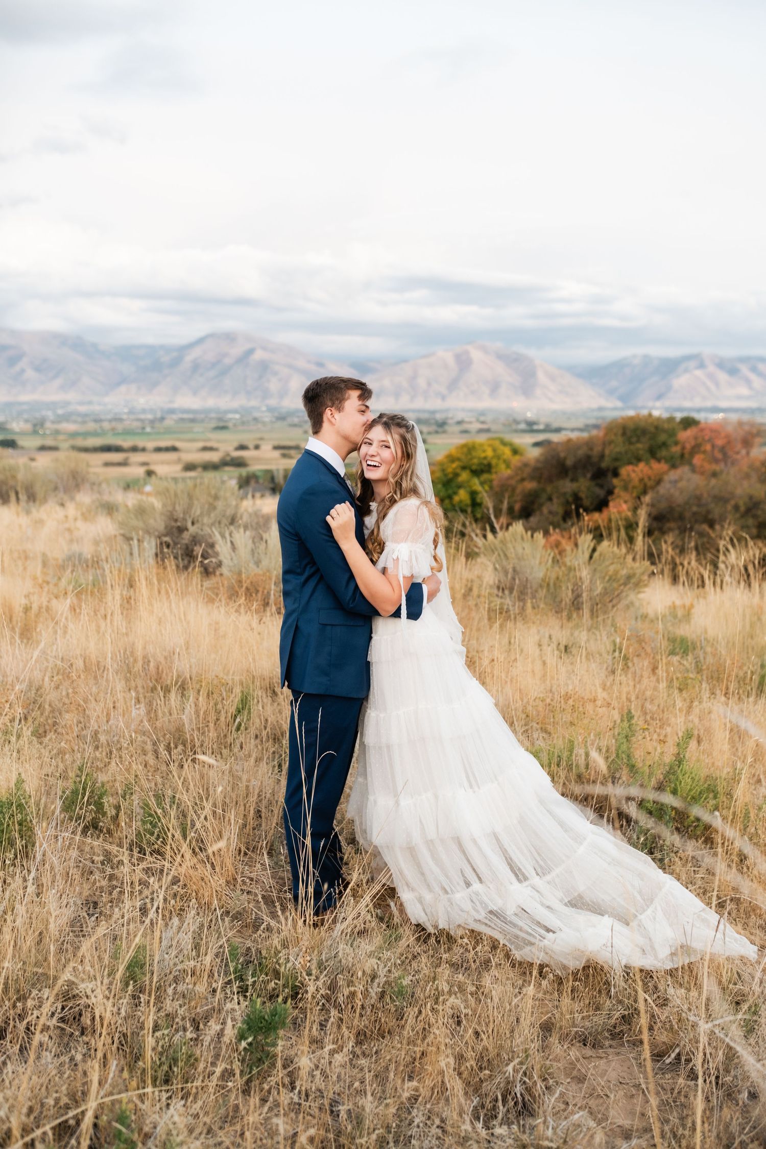 Golden prairie grass field with mountain range silhouetted against cloudy sky. Best Utah Wedding Photographers.