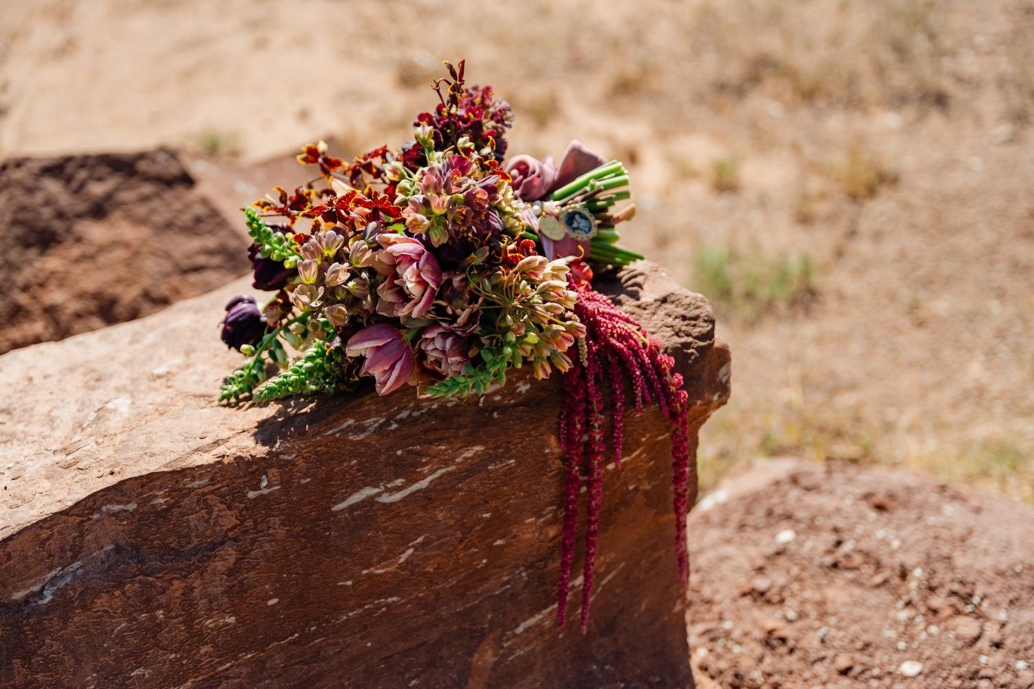 Colorful wildflower bouquet with red and green blooms resting on a rustic red rock in a dry desert landscape.
