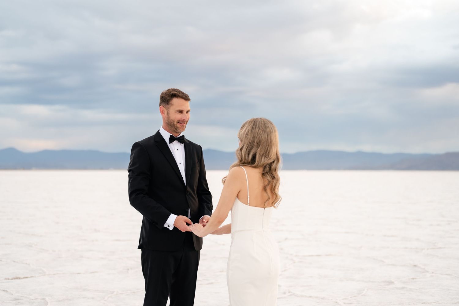 Salt Flats Elopement Photographer. A couple in wedding attire dances on the bright white salt flats against a cloudy sky.
