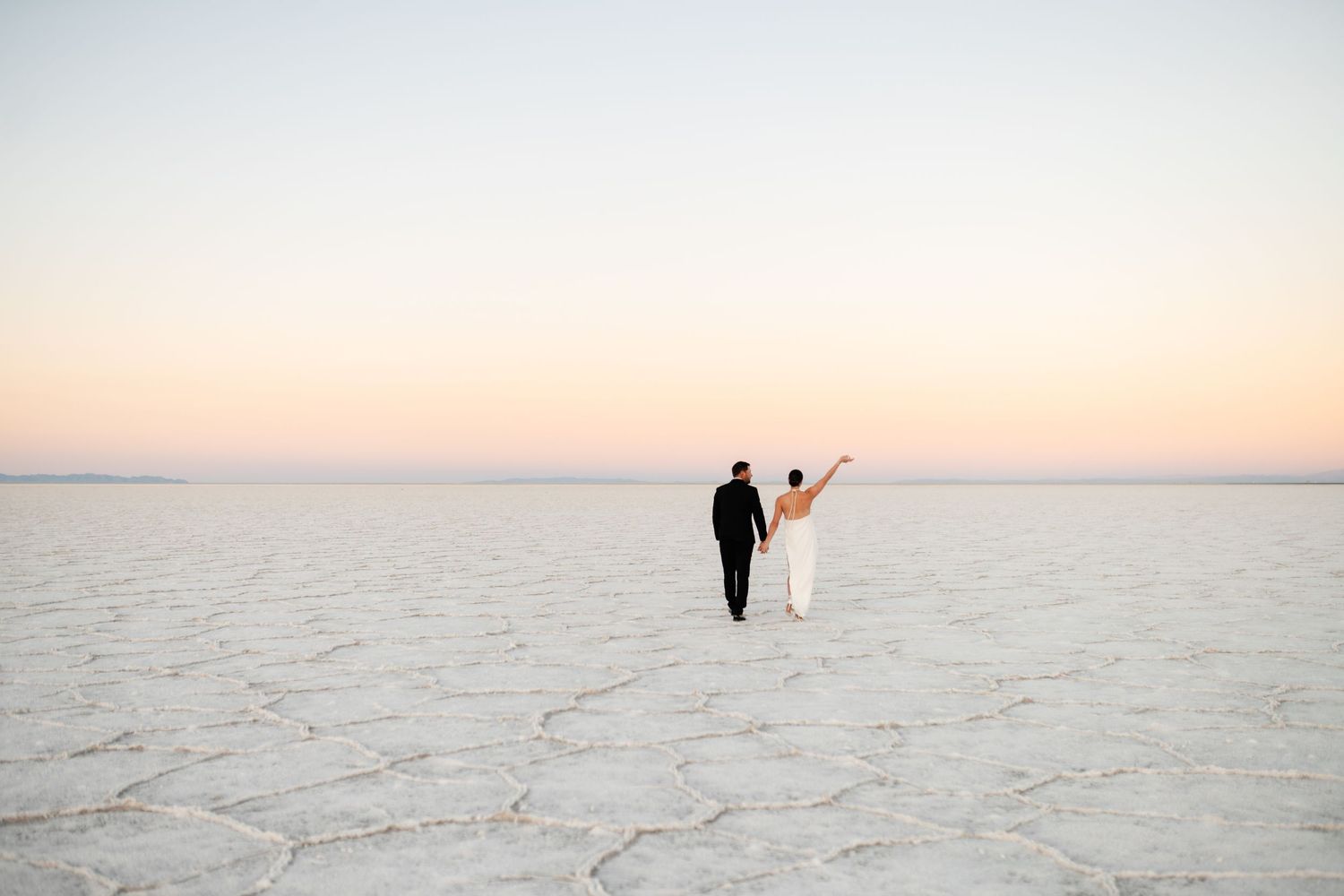 Utah Salt Flats Photographer. Two silhouettes walking together on a salt flat during sunset with a glowing orange sky.