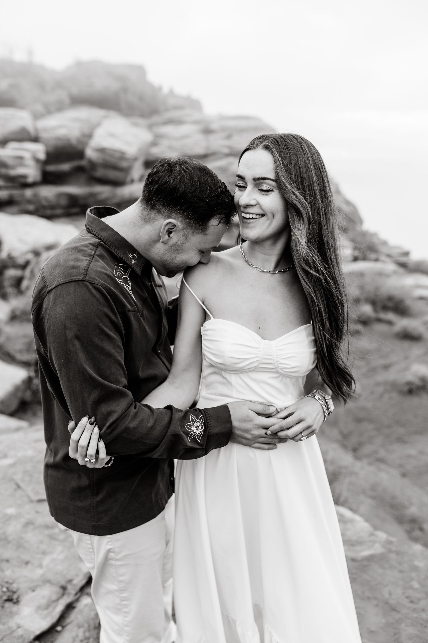 A romantic black and white photo series of a couple sharing intimate moments on desert rocks.