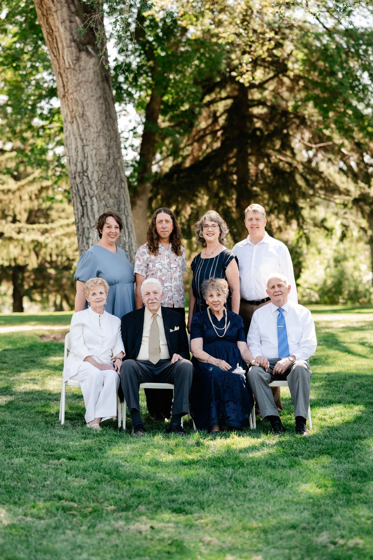 Family group sitting together on green grass in a park setting during a sunny day.