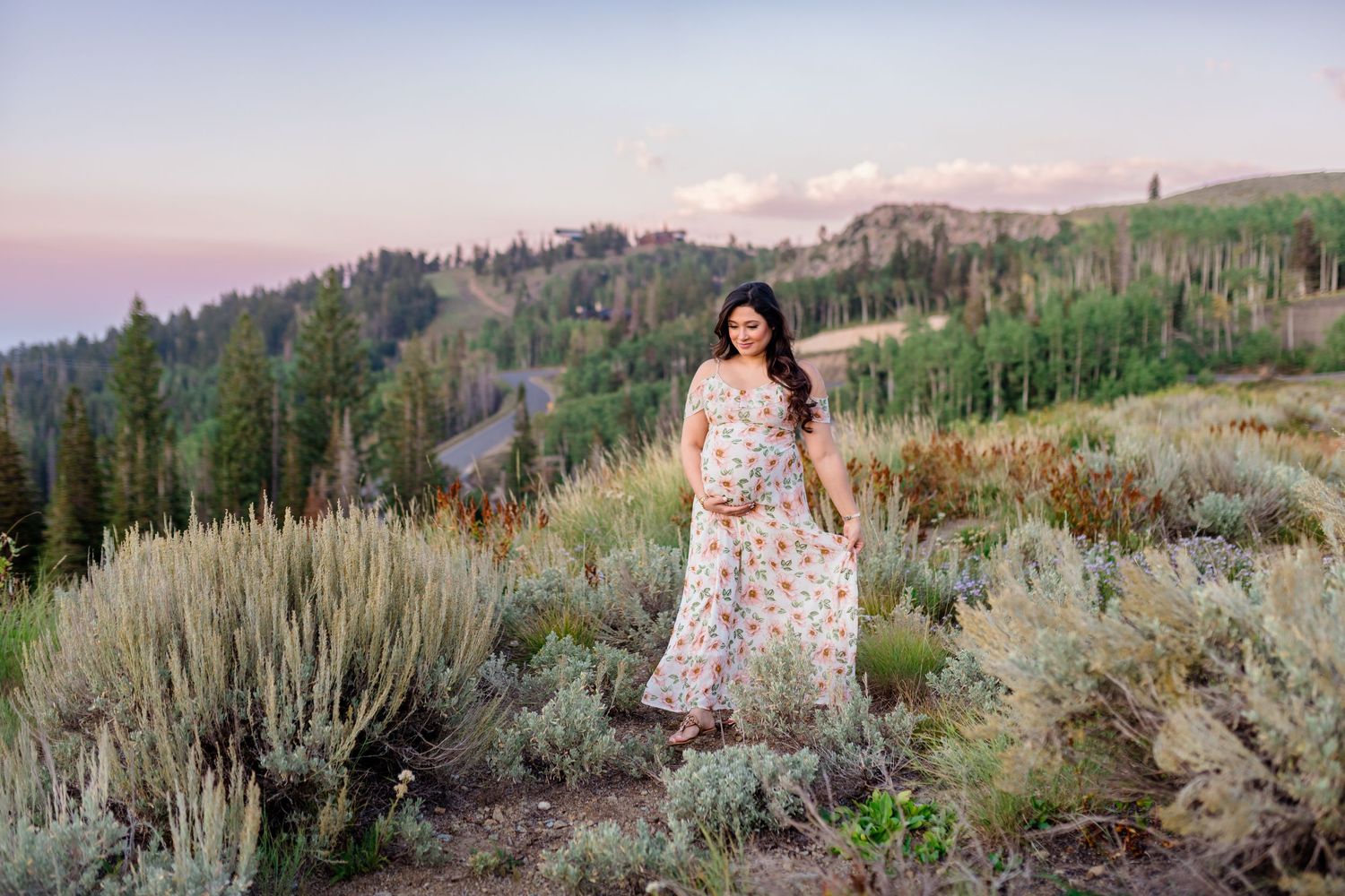 A figure in a floral dress poses among sagebrush and wildflowers in a mountain meadow at sunset.
