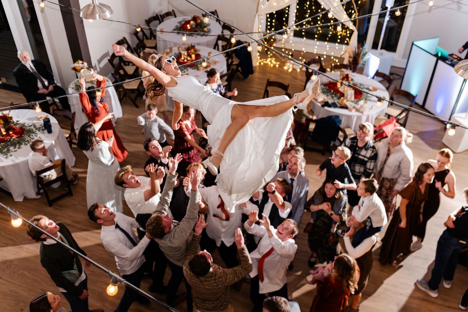 Bride tossed into air on a lively dance floor at an indoor reception venue with decorative lighting. Best Utah Wedding Photographers.