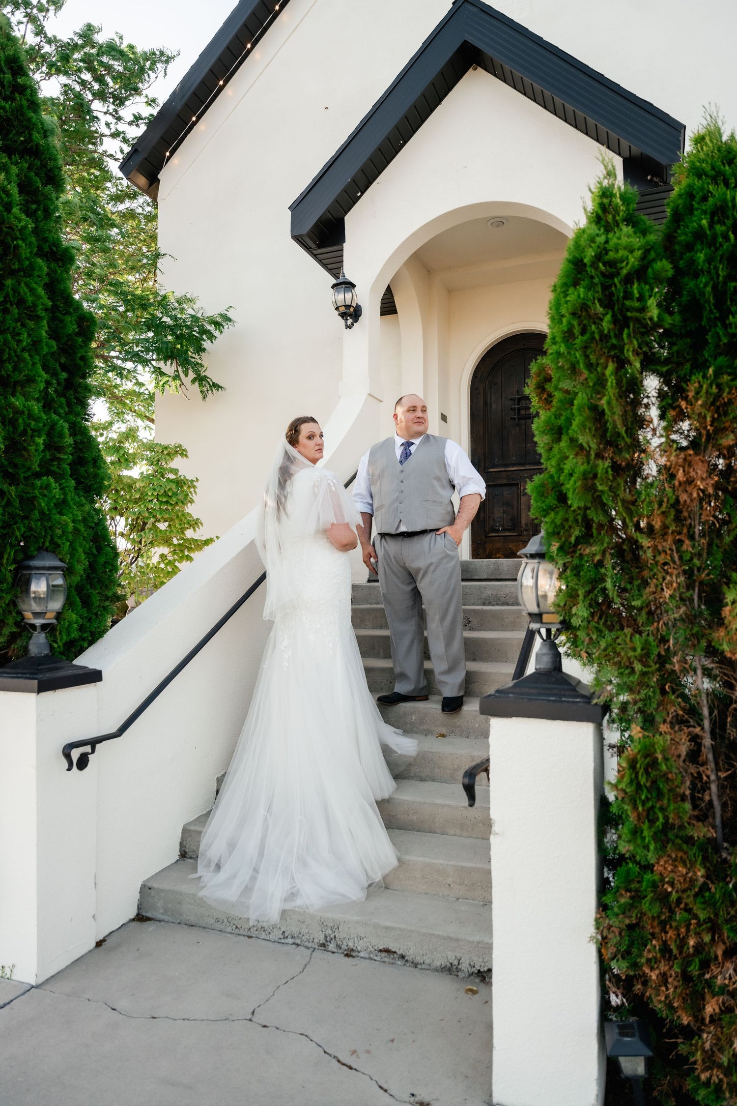 A couple stands together on white exterior steps of Stonegate Manor in Pleasant Grove. LDS wedding photographer.