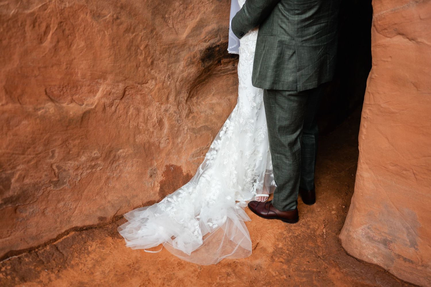 Wedding couple's feet standing on red desert sand with white dress flowing.
