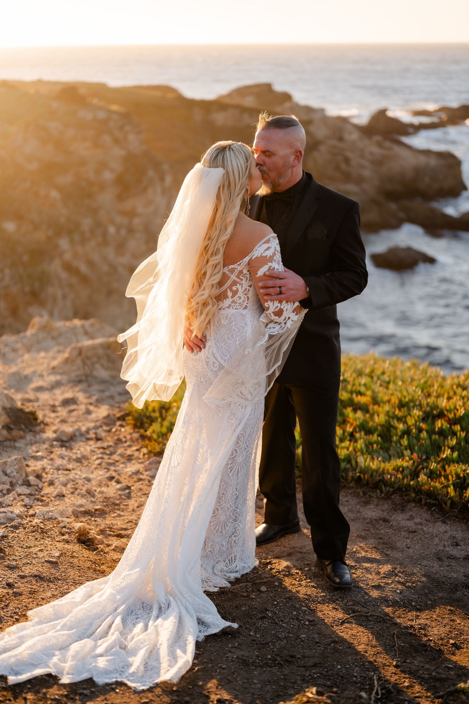 A couple shares an intimate moment on a coastal cliff during golden hour.