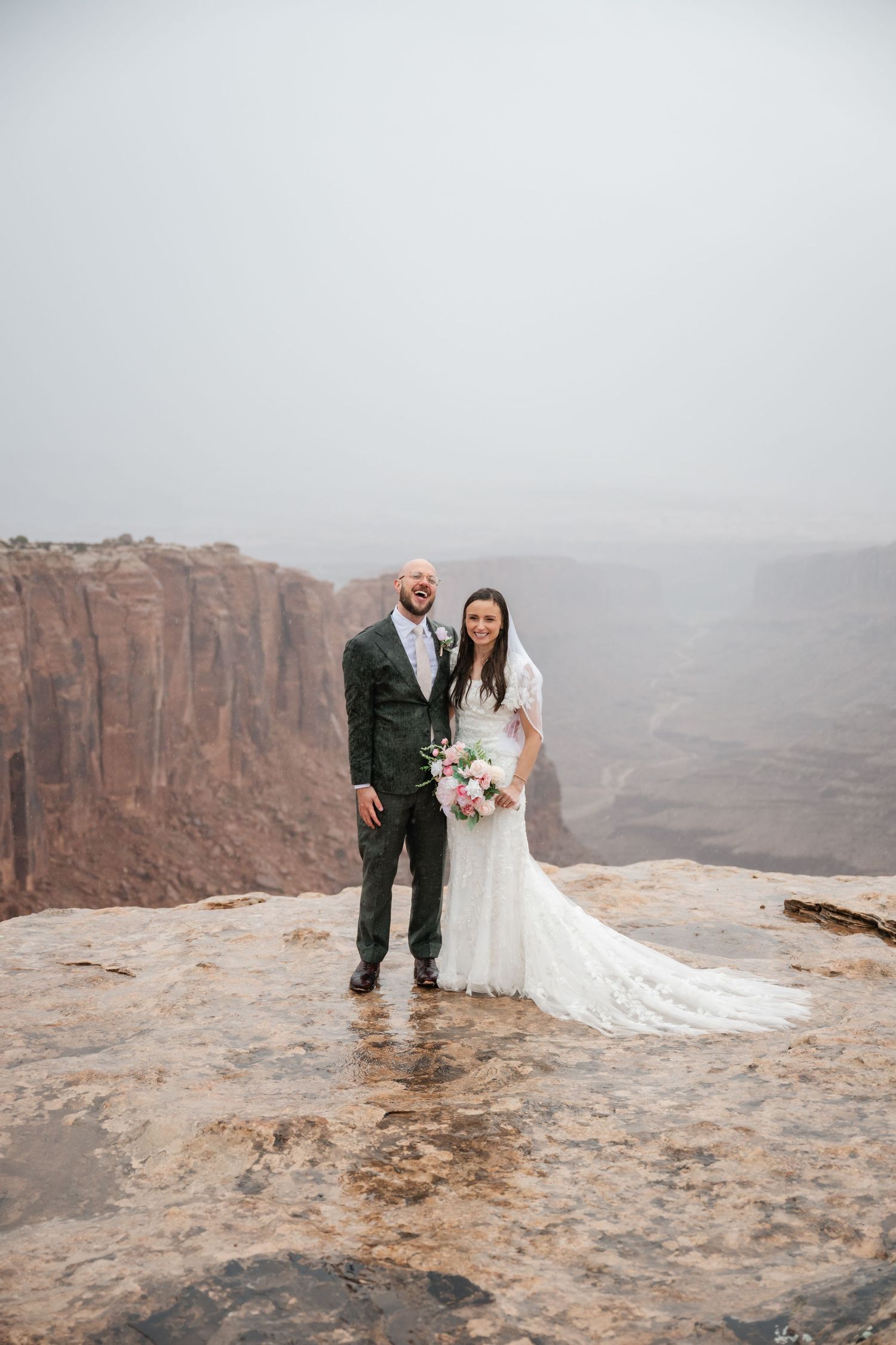 Intimate wedding ceremony against stunning canyon backdrop with long white wedding dress trailing on rocks.