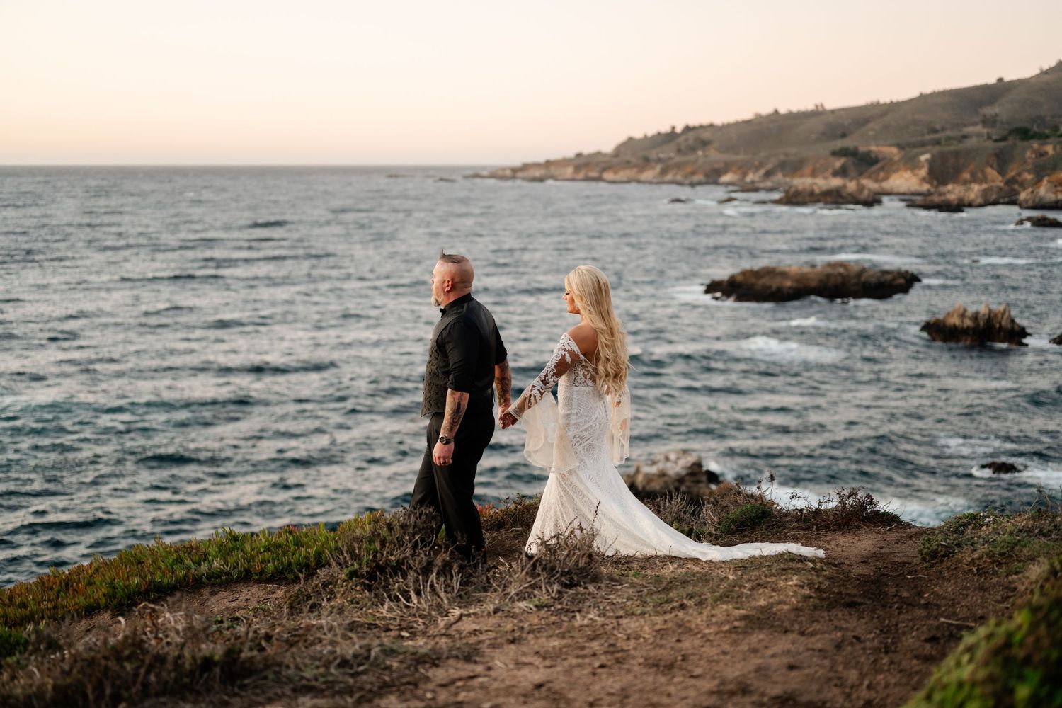 Dramatic wide-angle view of coastal wedding ceremony against mountainous ocean landscape.